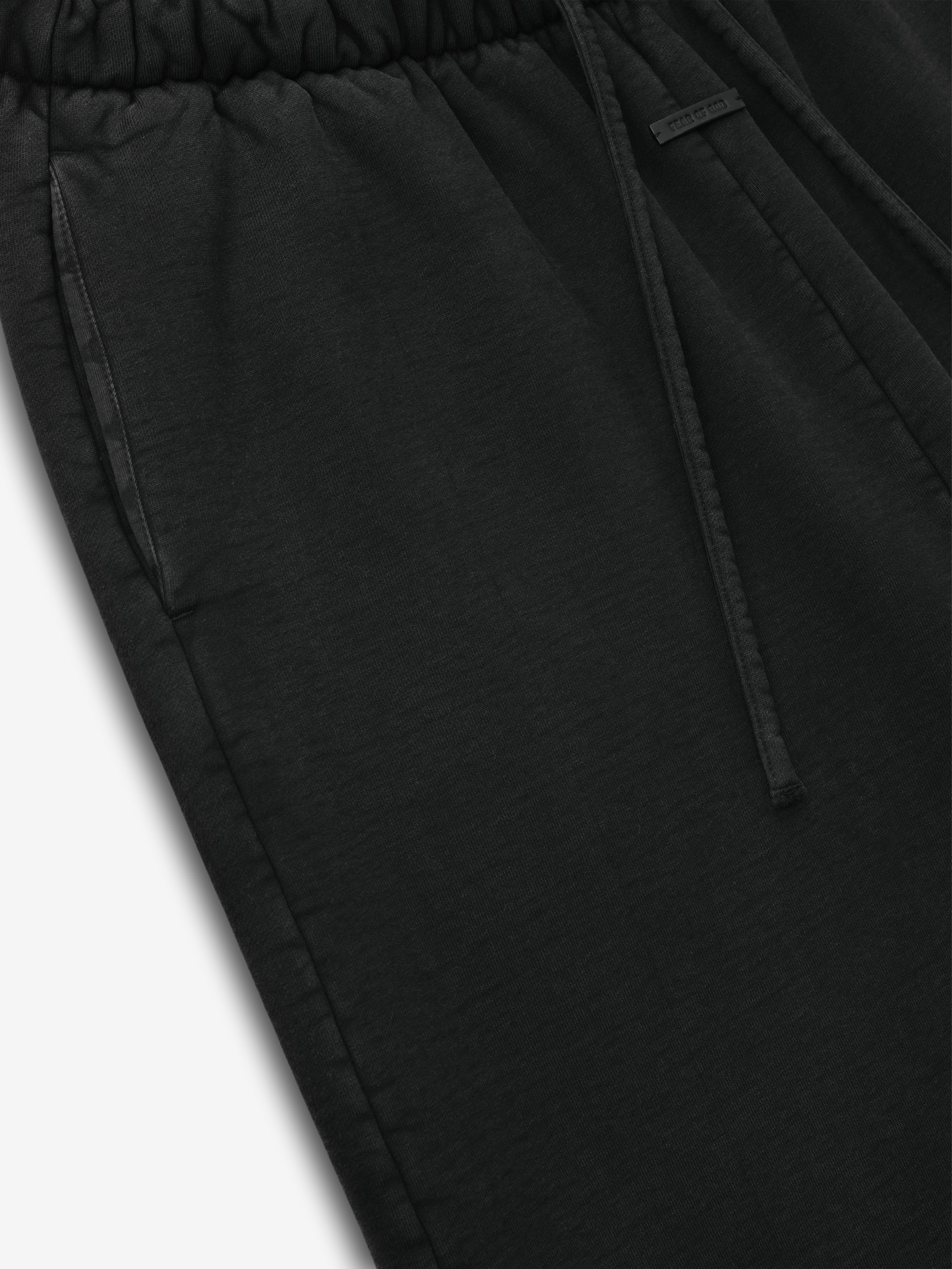 Close-up of black sweatpants with elastic waistband, side pocket, and drawstring detail on plain white background