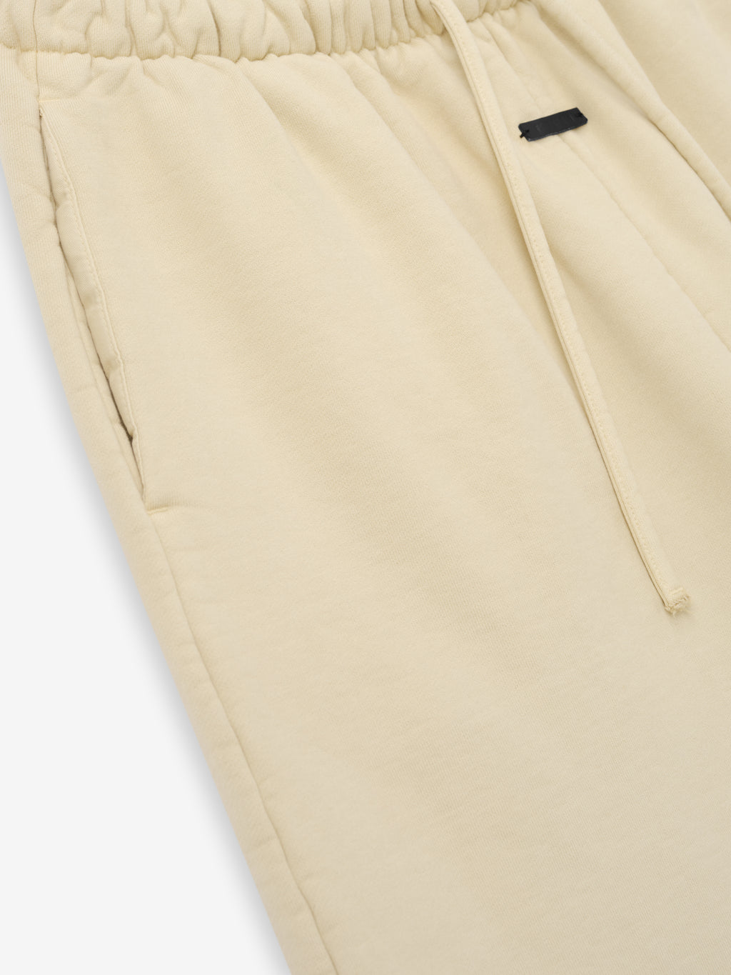 Close-up of light beige fleece pants with elastic waistband, drawstring, and side pocket detail on soft fabric surface