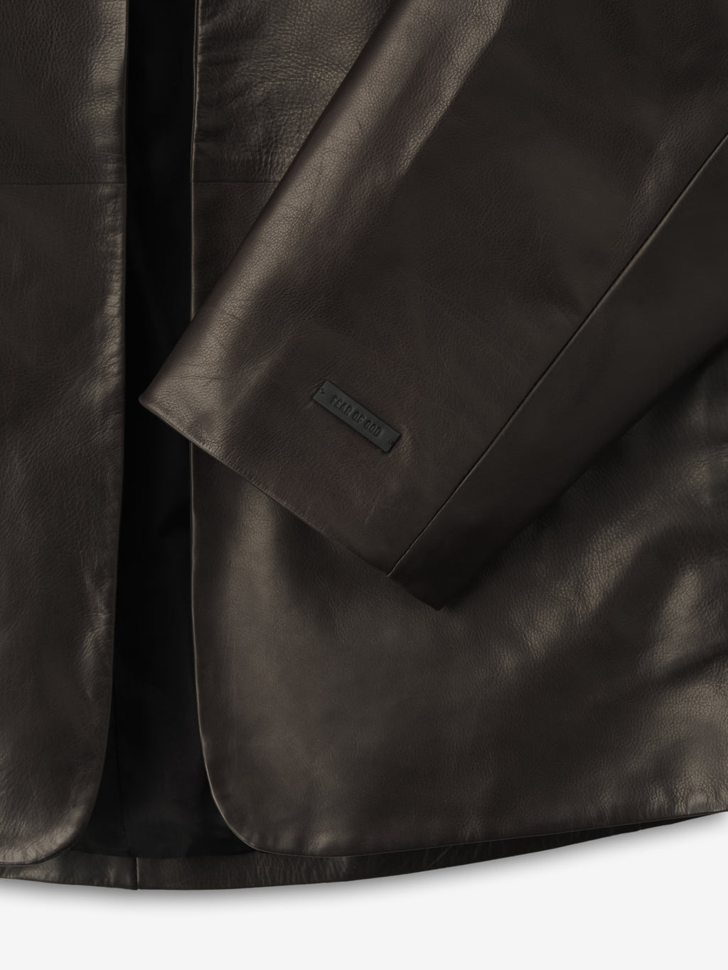 close-up of dark brown full-grain calfskin leather sleeve with embossed logo patch on women's collarless jacket
