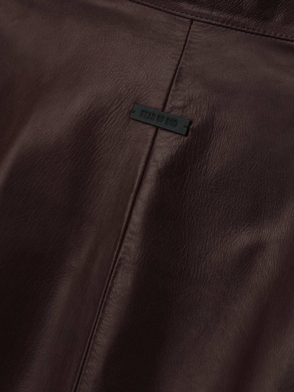close-up of dark brown full-grain calfskin leather panel with subtle seam and embossed logo patch on women's jacket