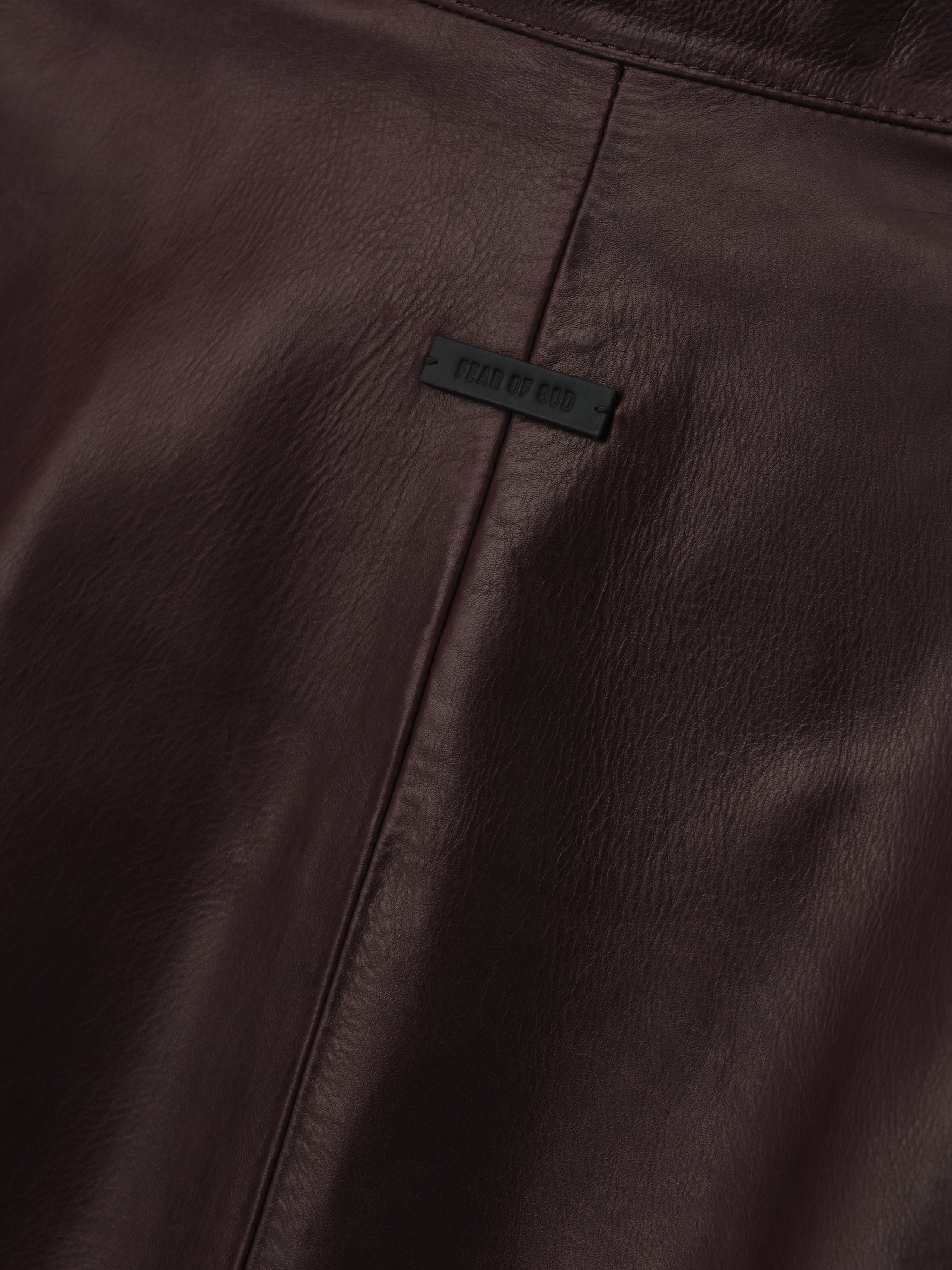 close-up of dark brown full-grain calfskin leather panel with subtle seam and embossed logo patch on women's jacket
