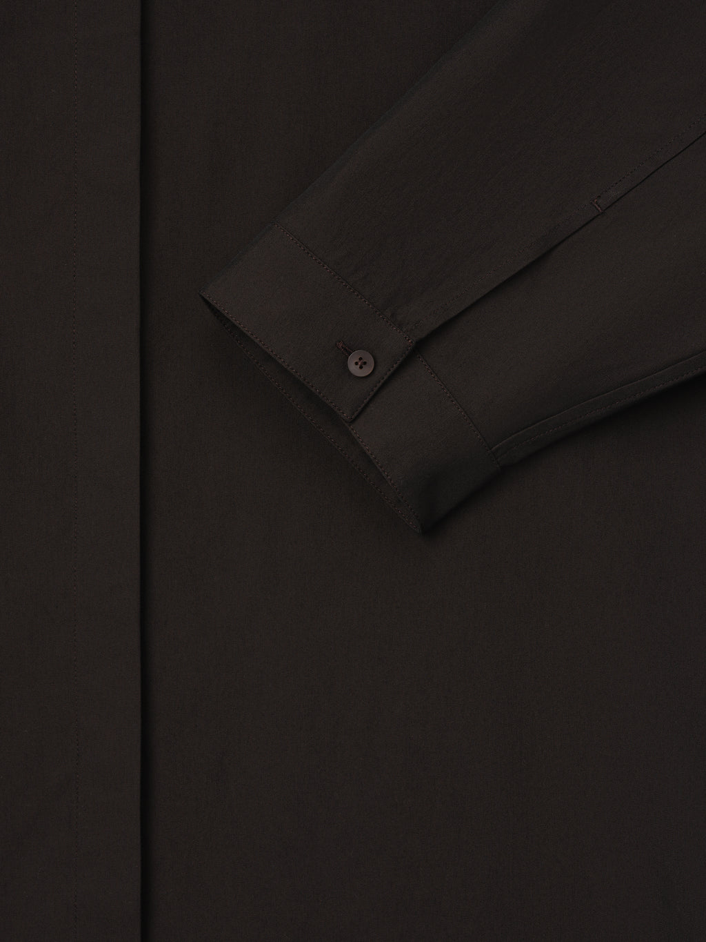 Close-up of dark brown shirt sleeve with buttoned cuff and smooth fabric texture on a plain background