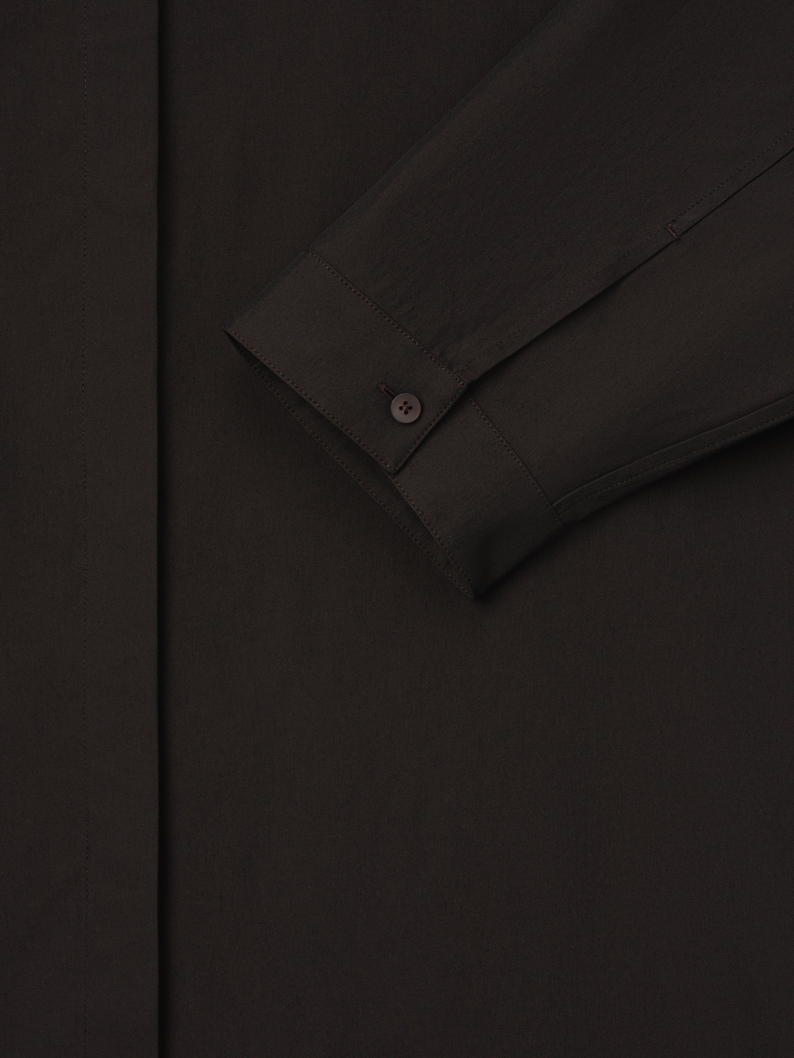 Close-up of dark brown shirt sleeve with buttoned cuff and smooth fabric texture on a plain background