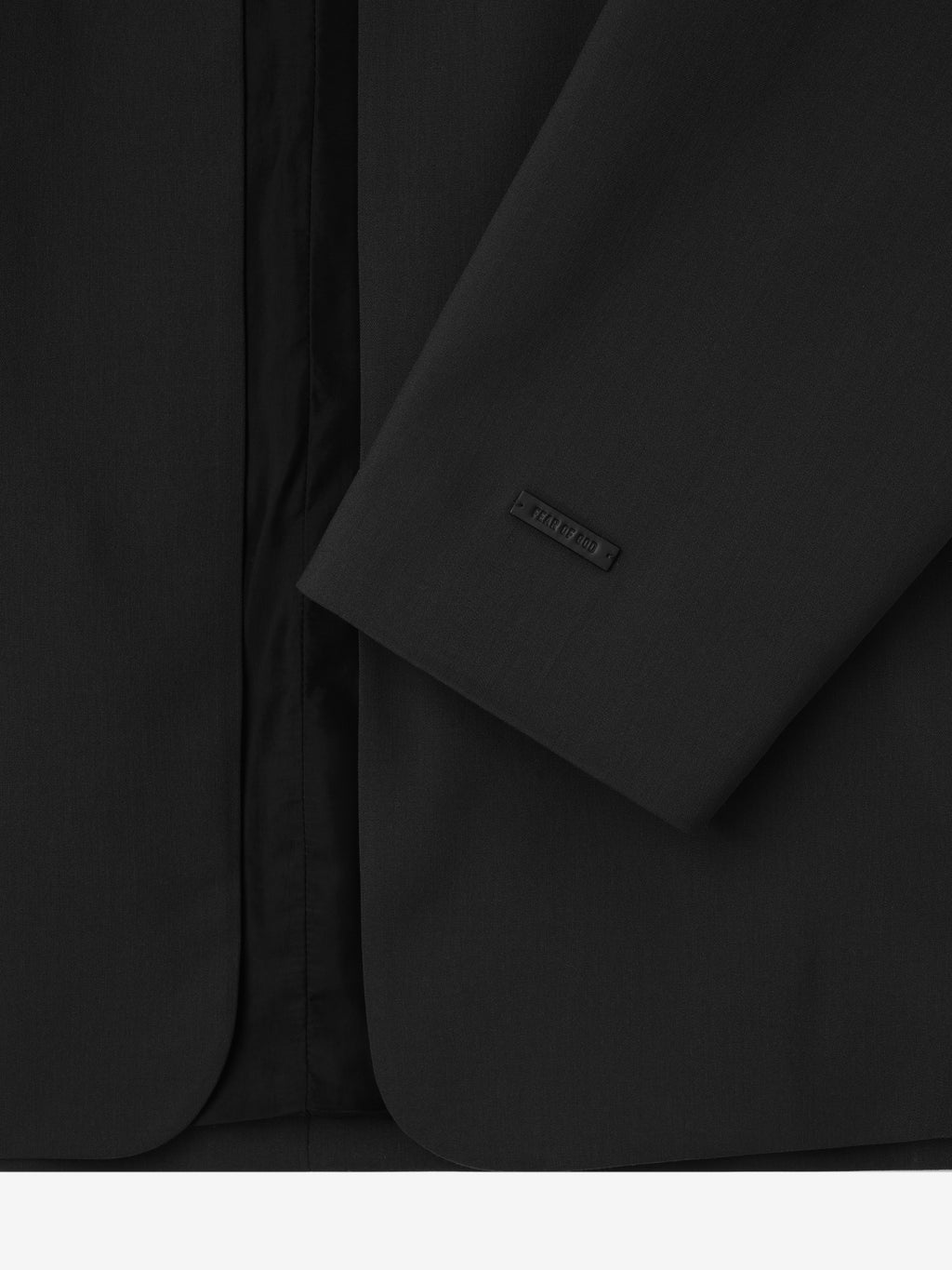 close-up of black collarless jacket sleeve with subtle branded tag and smooth, refined fabric texture