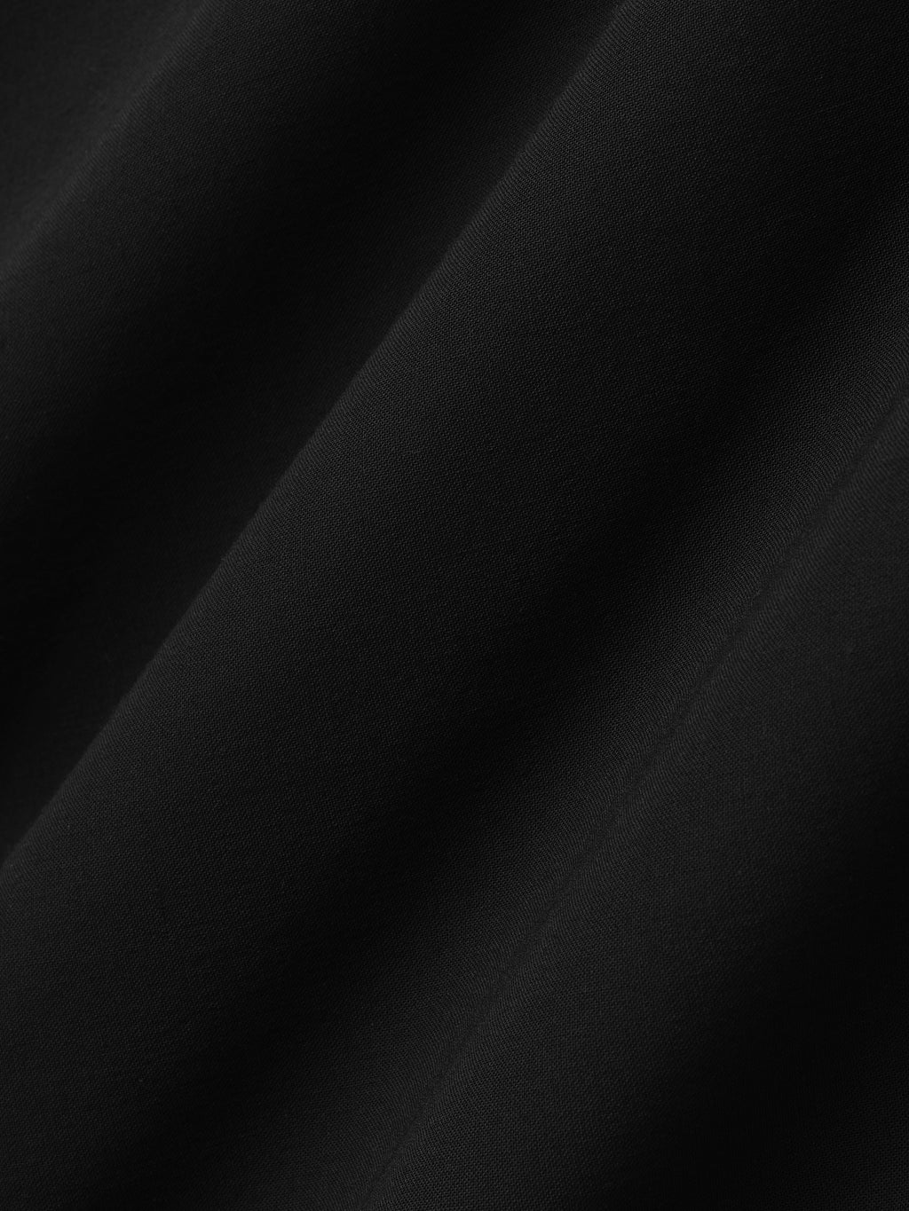 close-up of sheer black wool viscose fabric with smooth texture and subtle diagonal drape folds