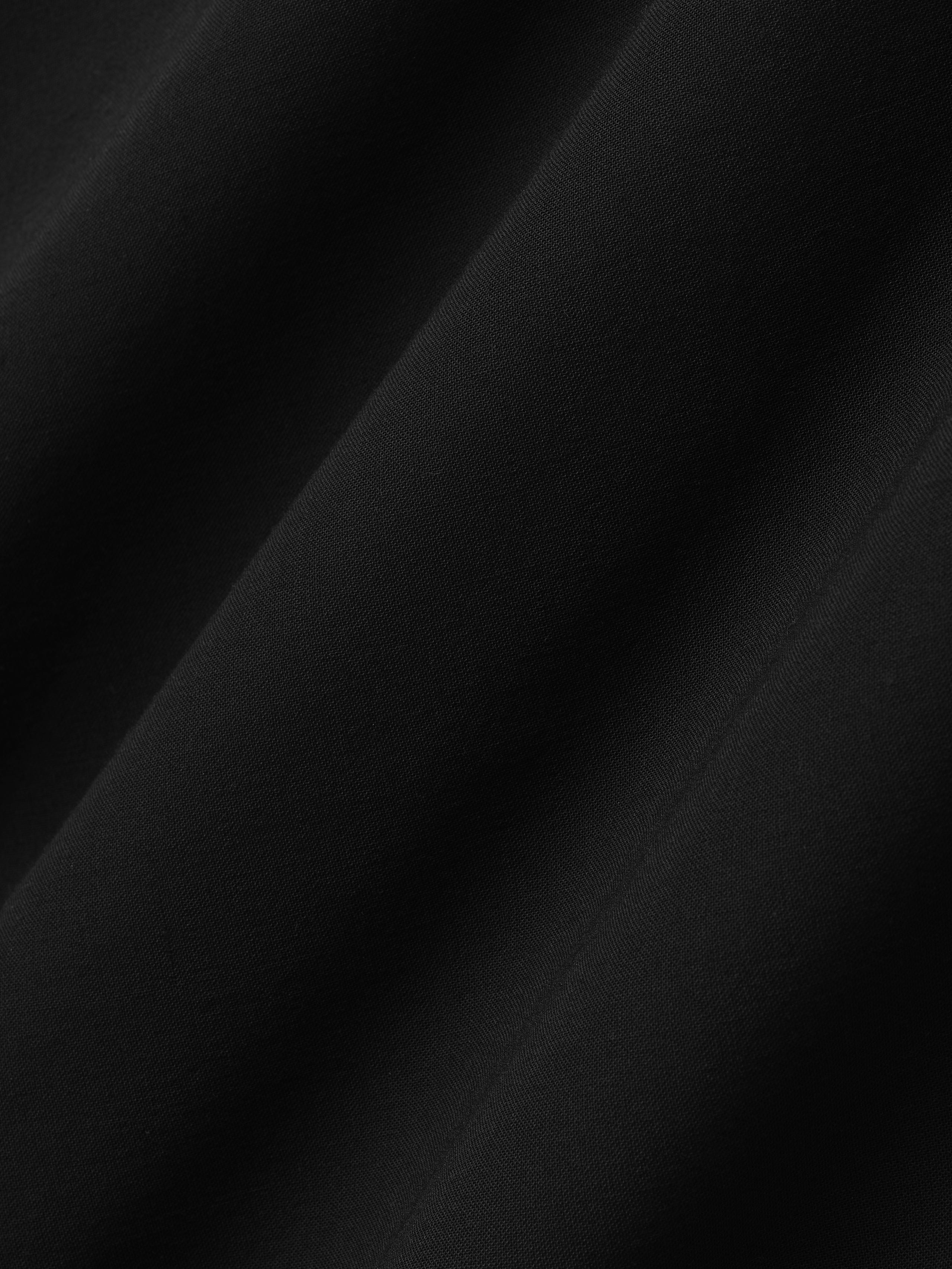 close-up of sheer black wool viscose fabric with smooth texture and subtle diagonal drape folds