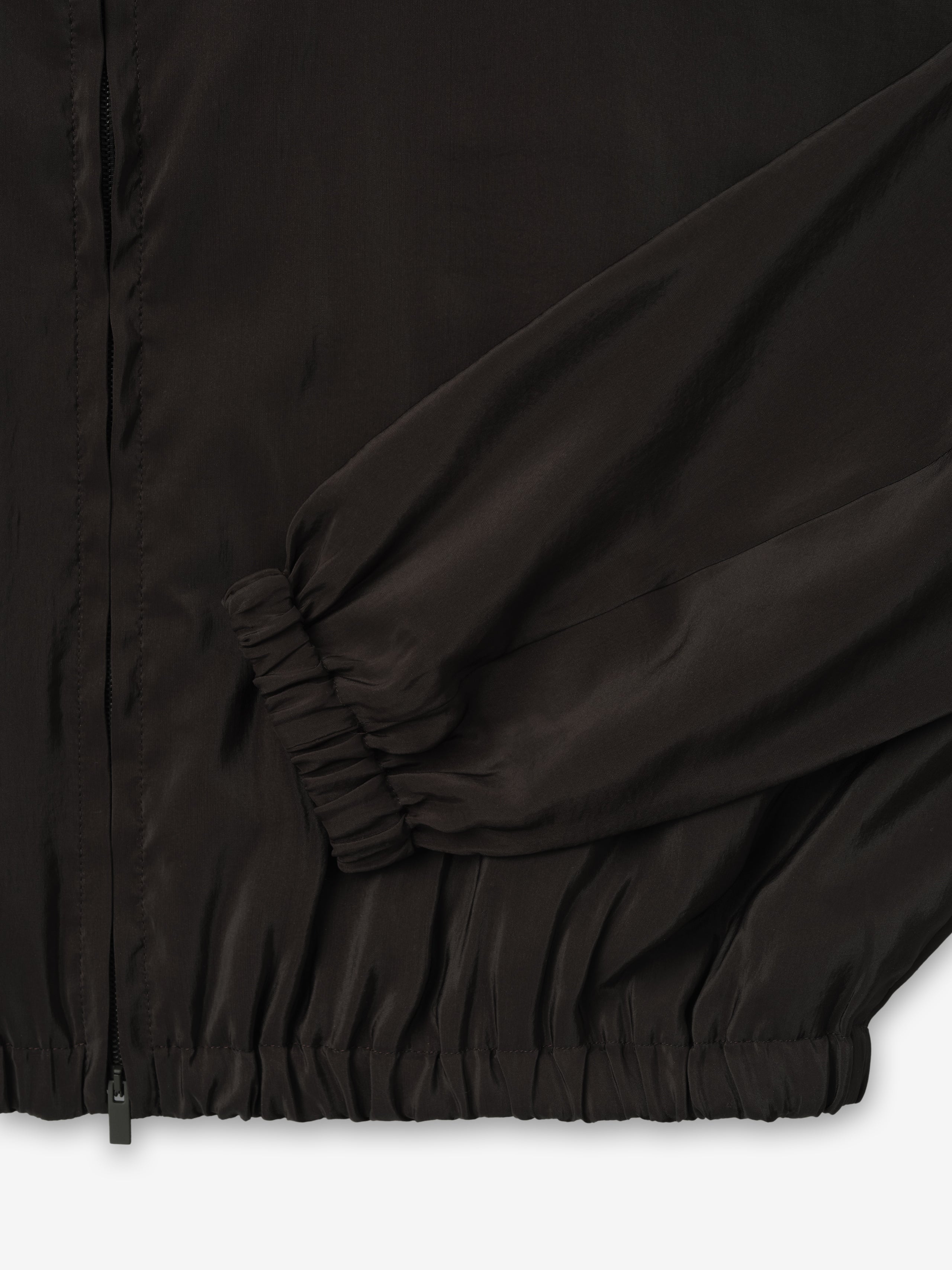 close-up of black lightweight crinkle viscose track jacket cuff and hem with elasticated ribbing and smooth matte finish