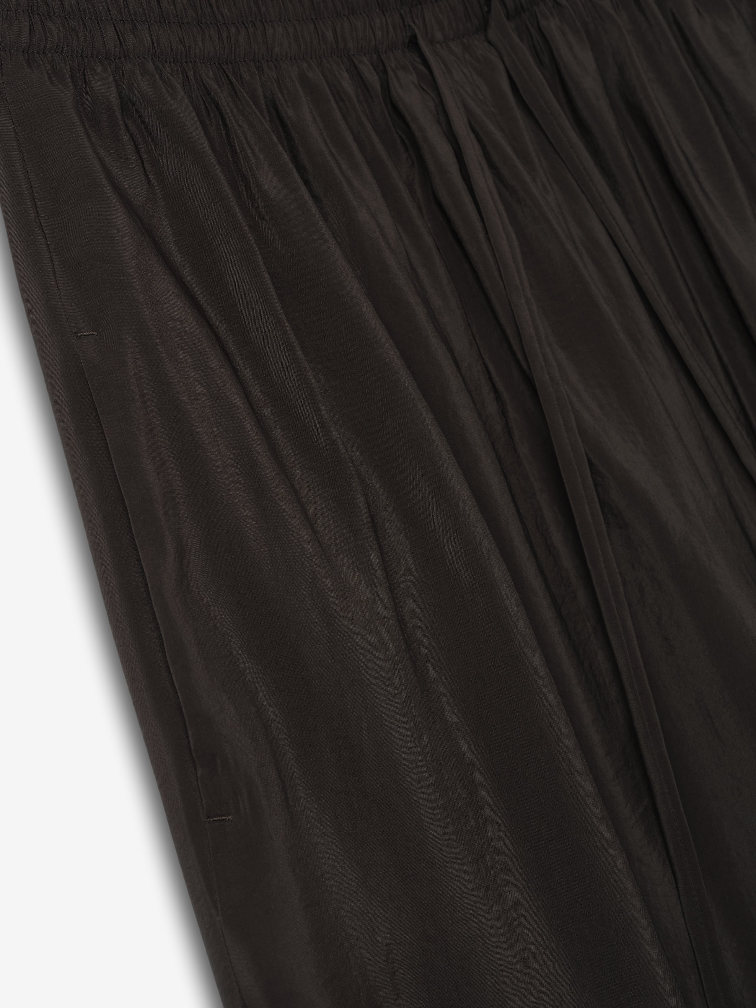 close-up of black crinkle viscose pants with elastic waistband and wide-leg drape in lightweight semi-sheer fabric
