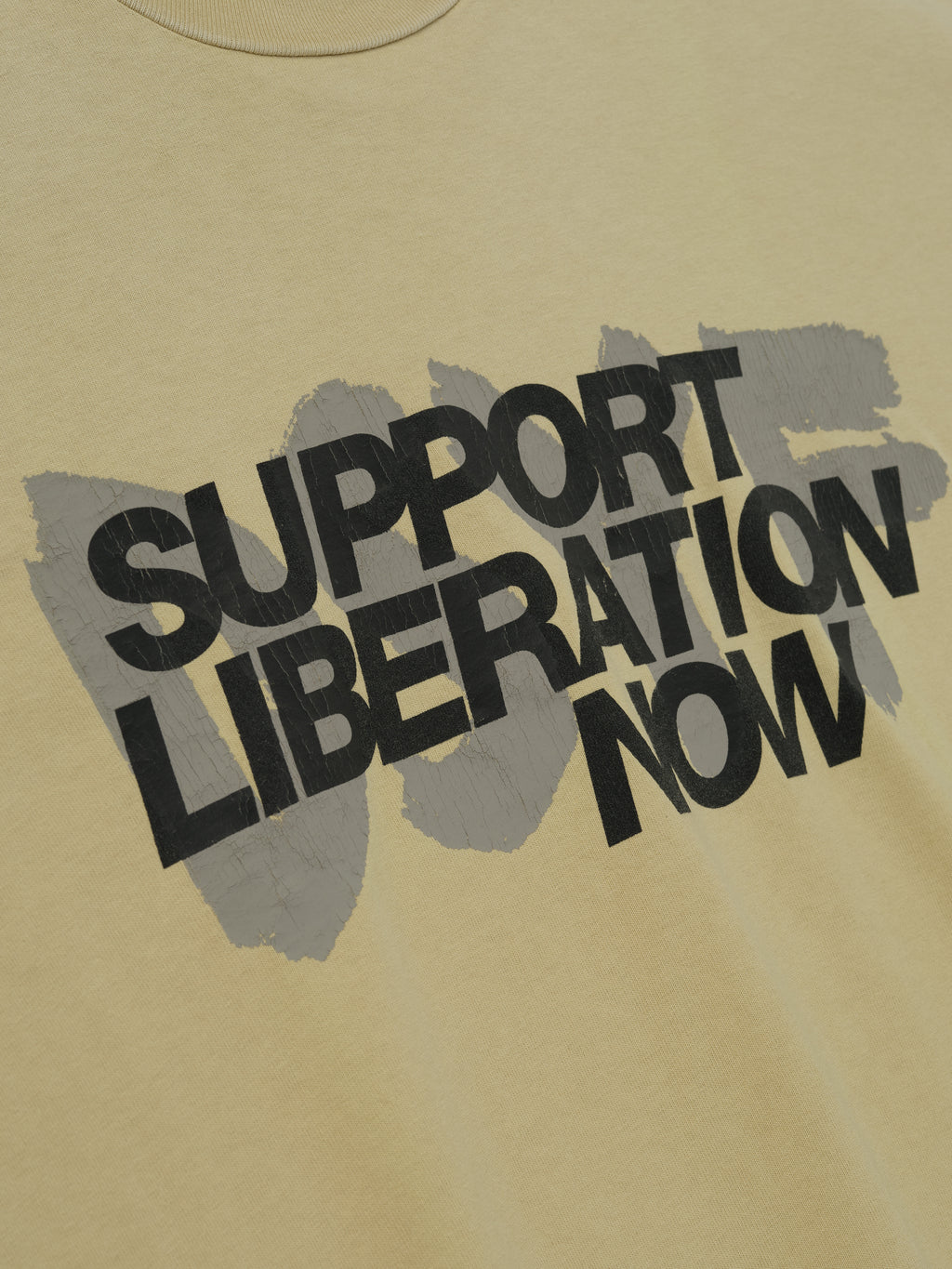 Close-up of clay Liberation Now Tee showing black "Support Liberation Now" text over gray brushstroke background centered on fabric