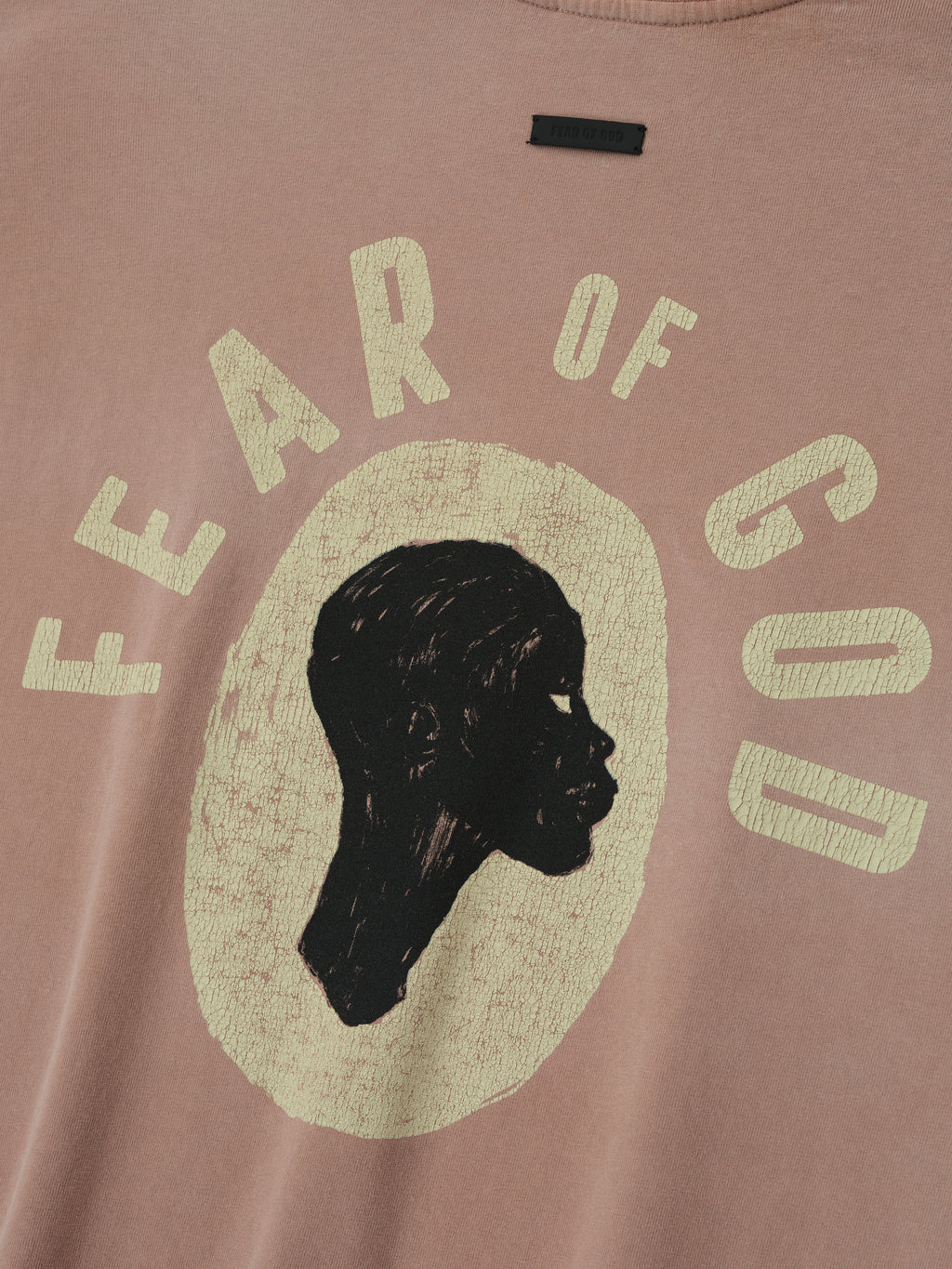 Close-up of dune pearl Liberation Now Tee featuring black profile silhouette and distressed pale yellow FEAR OF GOD text on chest
