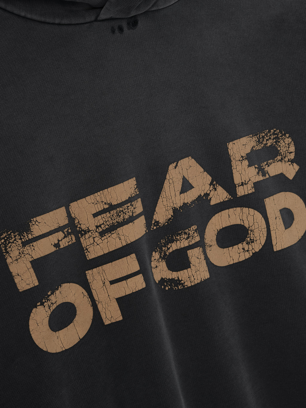 close-up of black cotton fleece hoodie with distressed beige "FEAR OF GOD" hand-printed graphic text