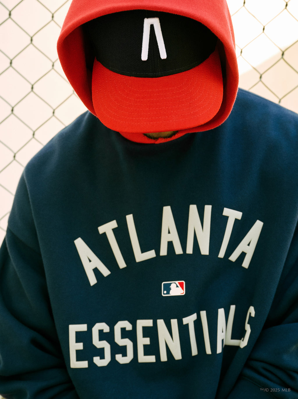 Navy blue hoodie with white "ATLANTA ESSENTIALS" text and small MLB logo worn by person in red and black cap