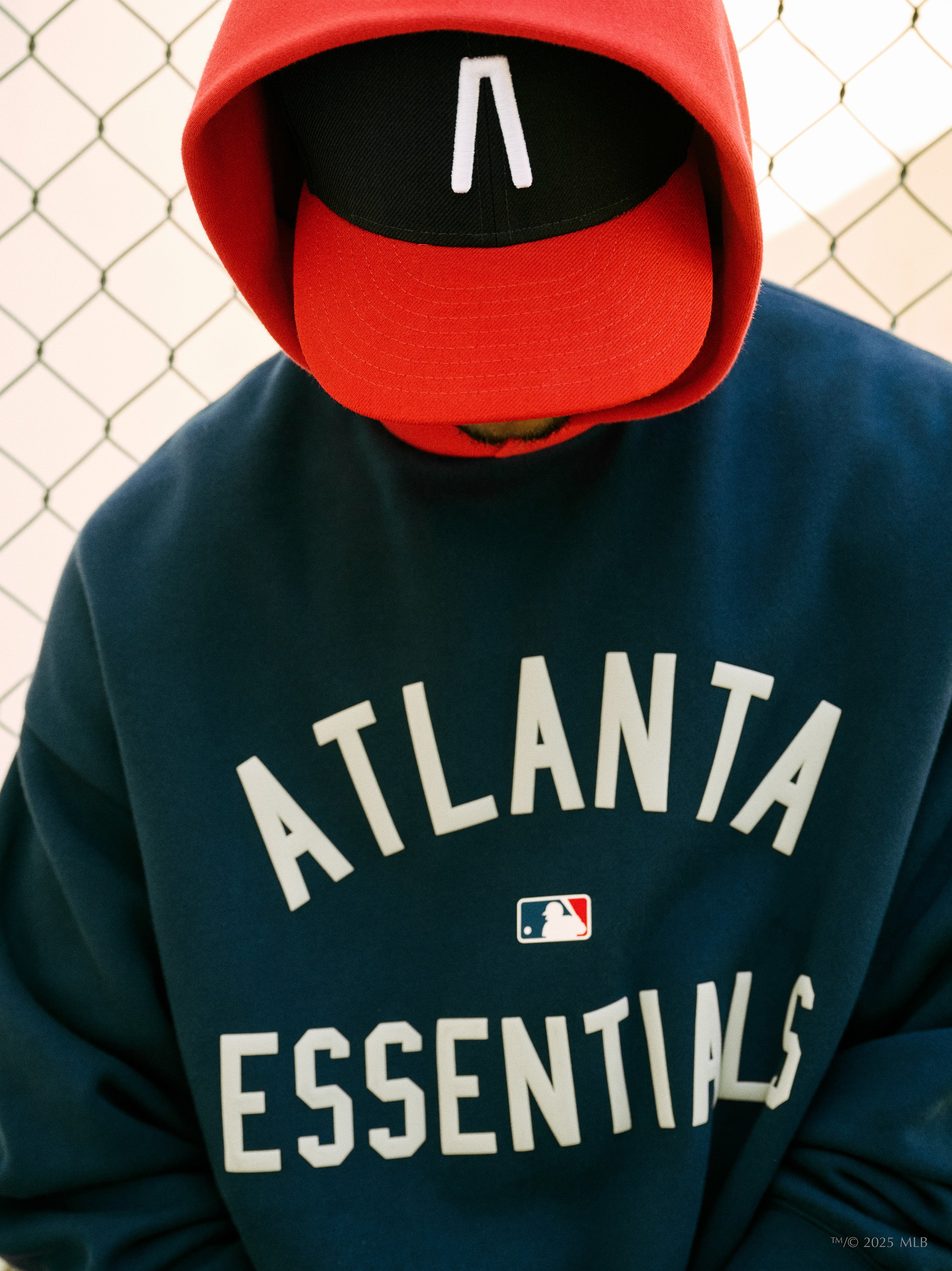 Navy blue hoodie with white "ATLANTA ESSENTIALS" text and small MLB logo worn by person in red and black cap