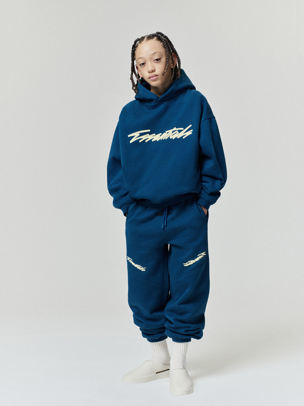 Kids Classic Raglan Hoodie in navy blue styled on a child model with a script chest graphic and matching jogger pants as Tops