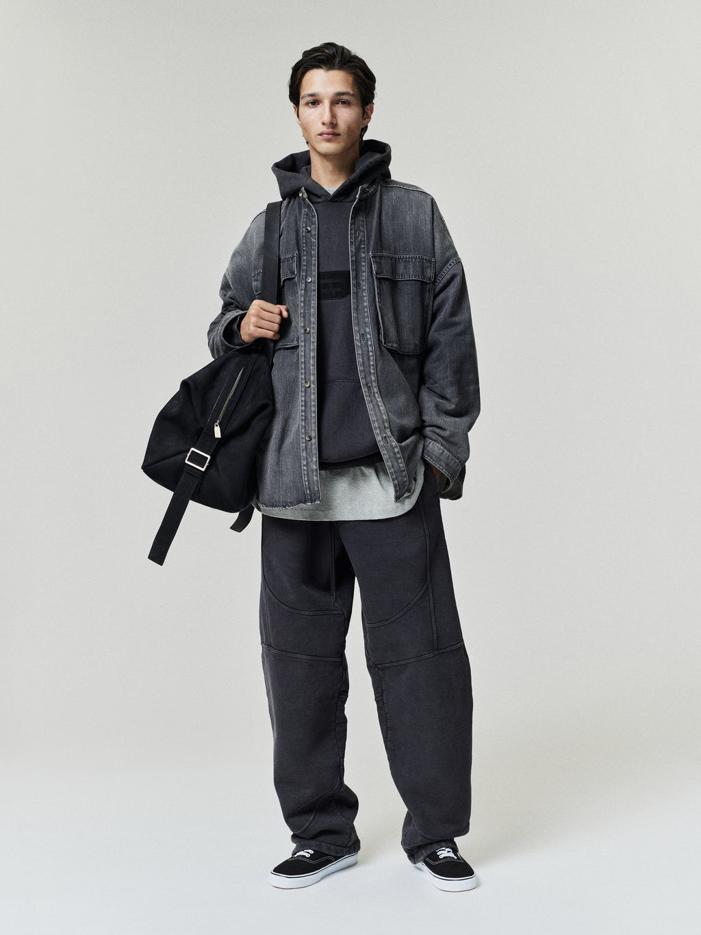 Slouchy 90s Hoodie modeled in charcoal beneath a washed black denim overshirt with relaxed dark trousers a shoulder bag and sneakers Tops
