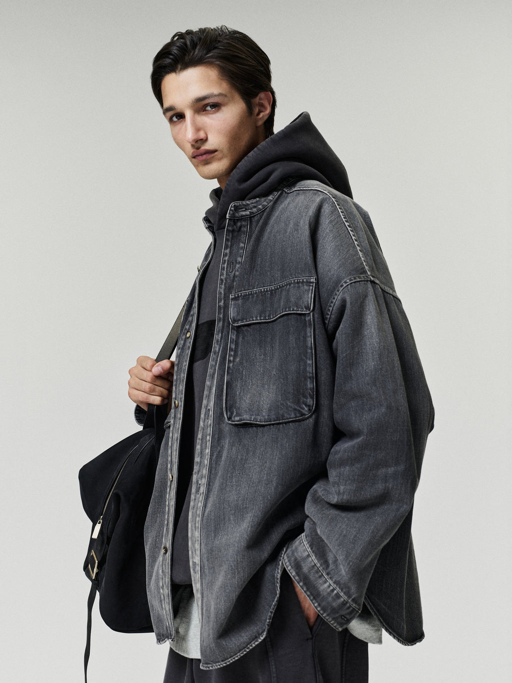 Slouchy 90s Hoodie modeled in black beneath a washed gray denim overshirt with a shoulder bag and relaxed styling Tops