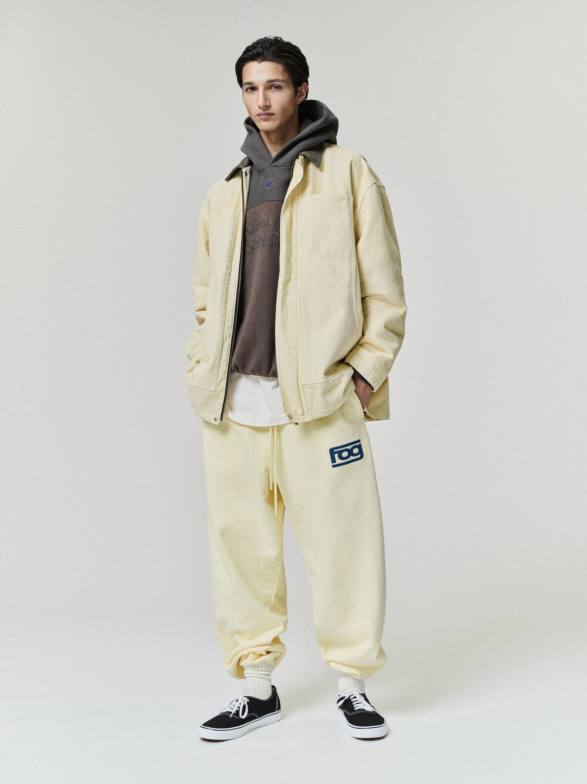 Browns 90s Relaxed Hoodie in dark brown layered under a cream jacket with matching relaxed pants and black sneakers on a model as a Tops fashion view