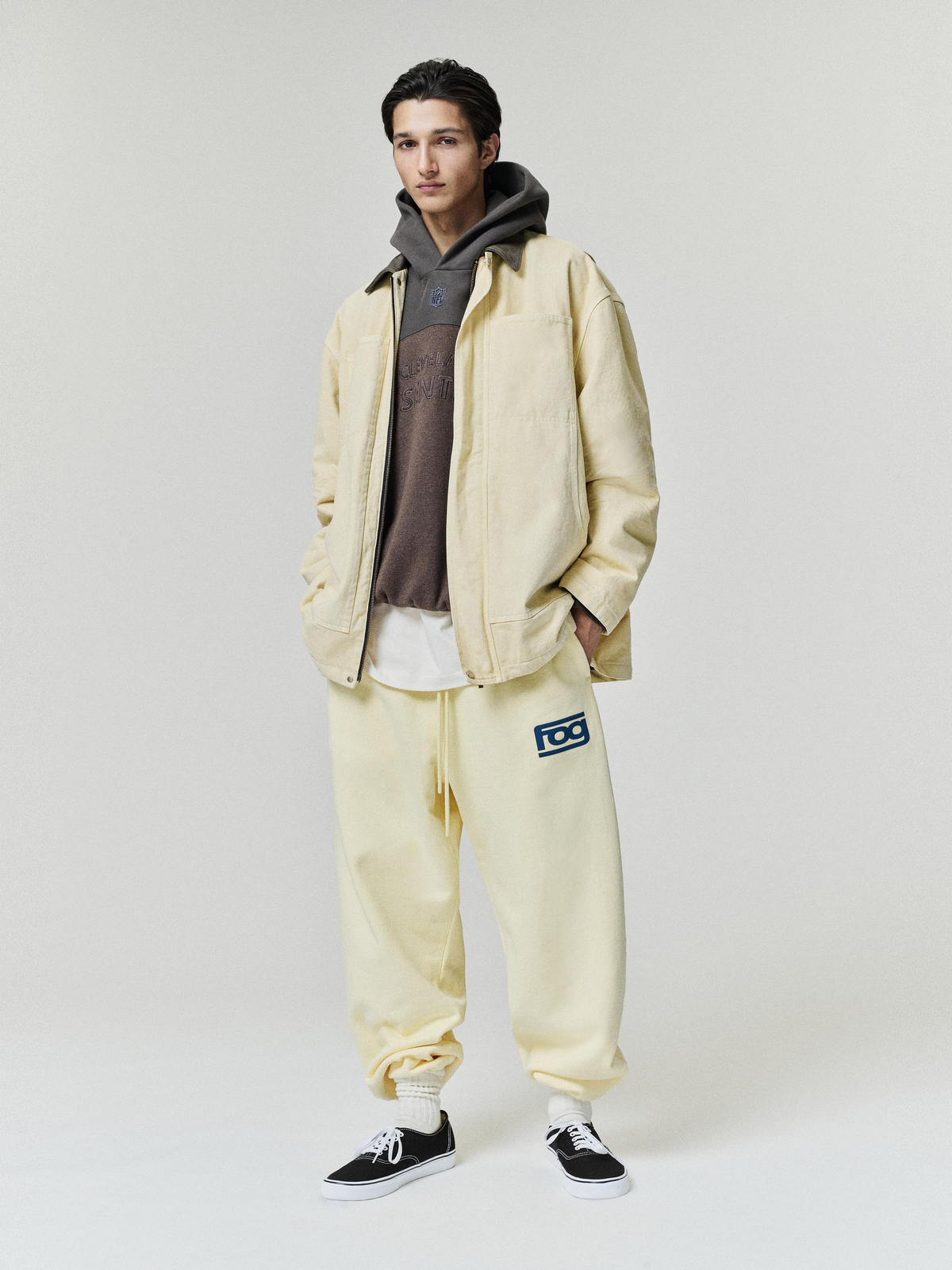 Browns 90s Relaxed Hoodie worn by a model under a cream jacket with matching joggers and black sneakers in a studio as Tops