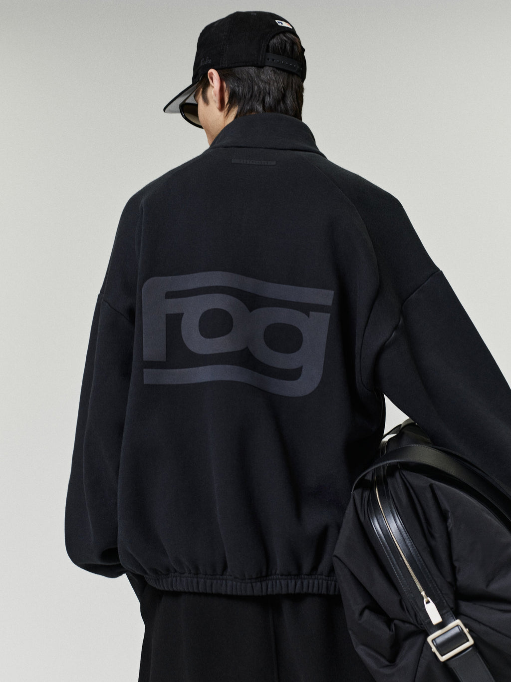 Classic Track Jacket in black shown from the back on a model with a tonal oversized logo and black shoulder bag as Outerwear