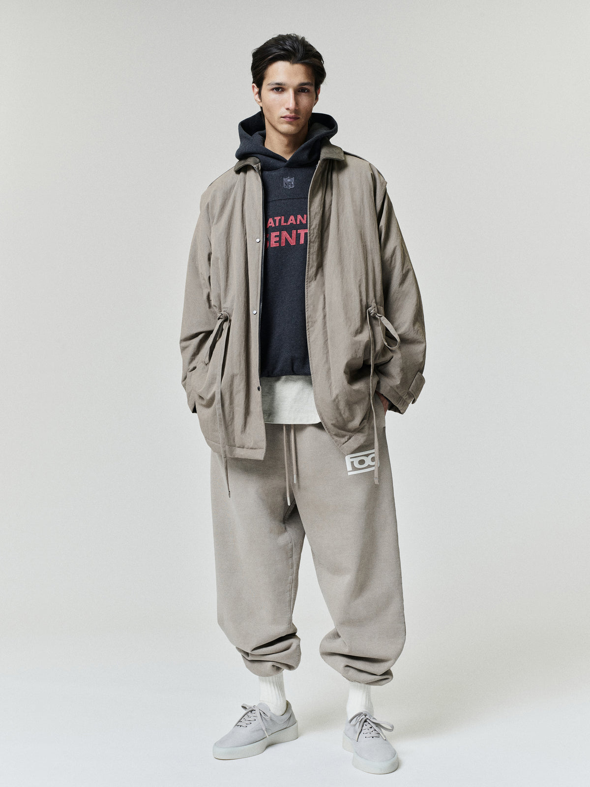 Falcons 90s Relaxed Hoodie layered under a taupe jacket with relaxed trousers and white sneakers on a model as a Tops fashion view