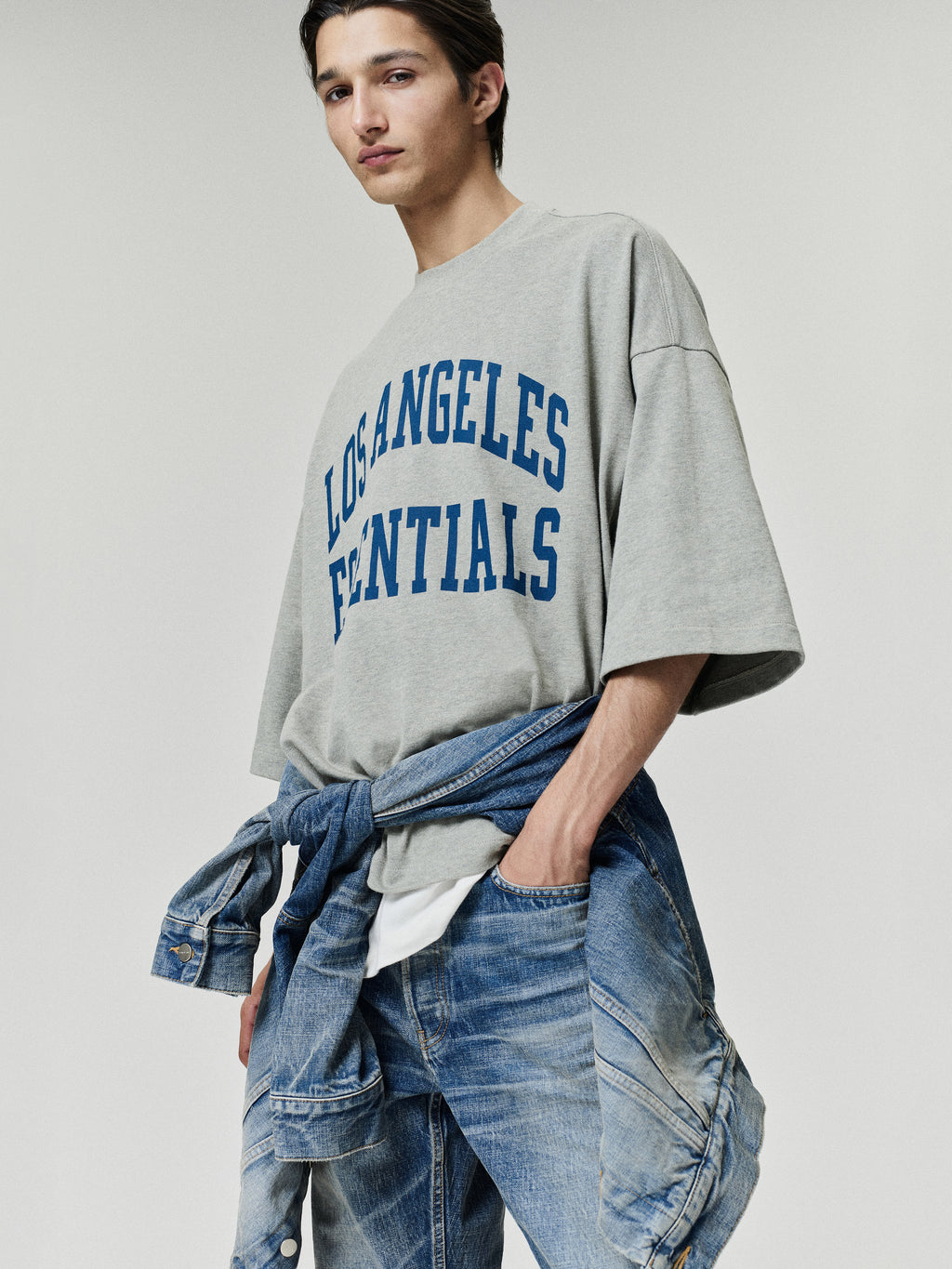 Rams Merch Tee gray oversized short sleeve shirt with blue Los Angeles Essentials collegiate lettering styled on a model with layered denim in a casual Tops look