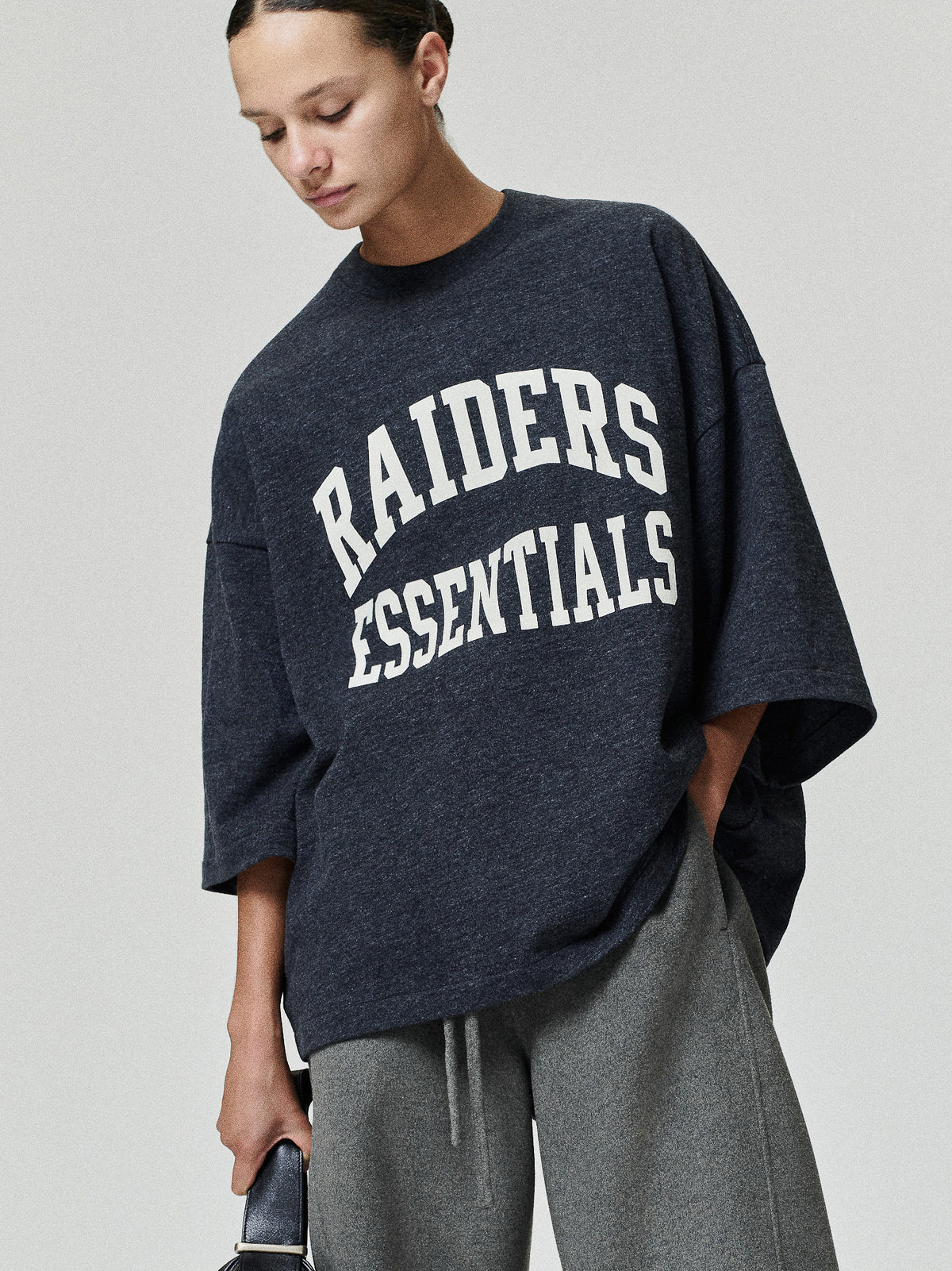 Raiders Merch Tee charcoal oversized short sleeve shirt with white Raiders Essentials collegiate lettering styled on a model in a casual Tops look