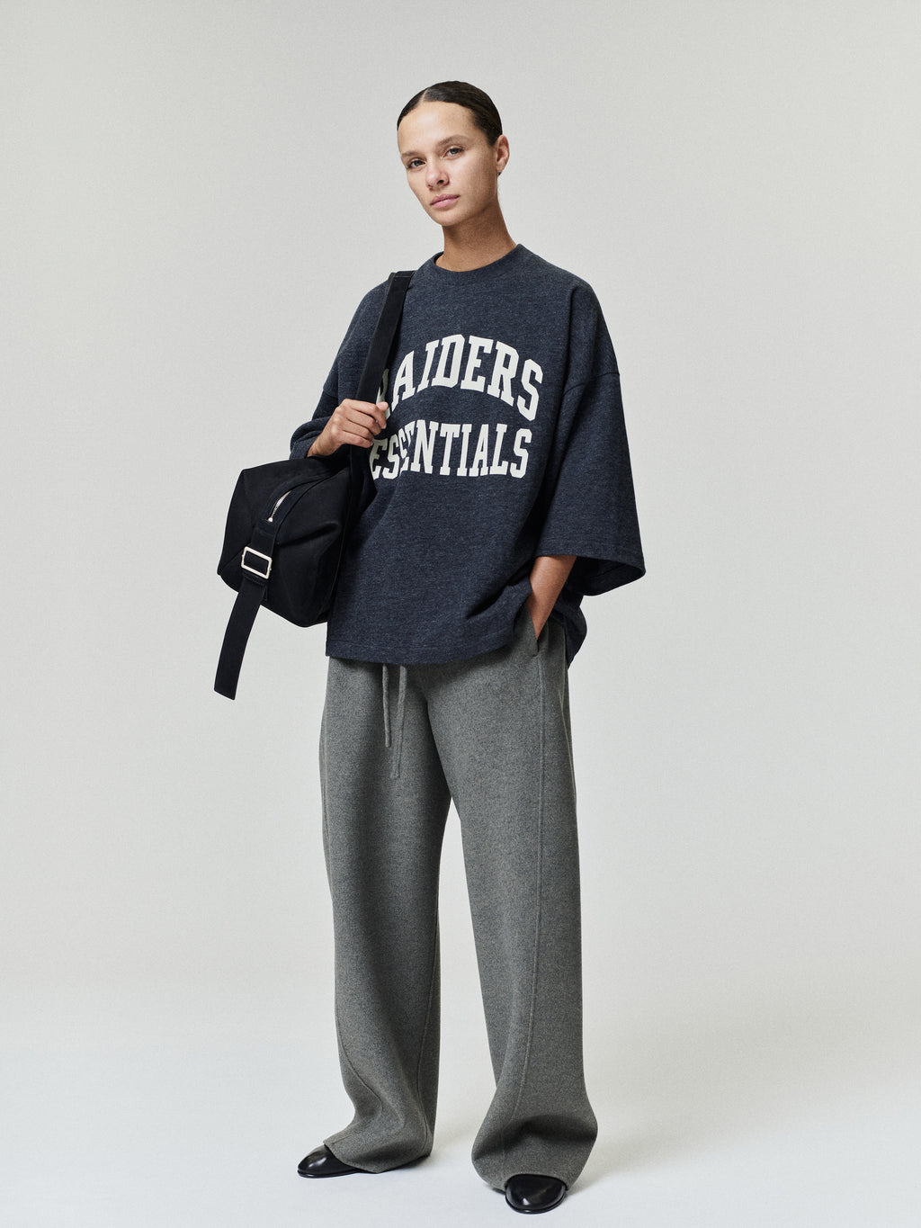 Raiders Merch Tee charcoal oversized short sleeve shirt with white Raiders Essentials collegiate lettering styled with wide leg gray pants and a shoulder bag in a Tops look
