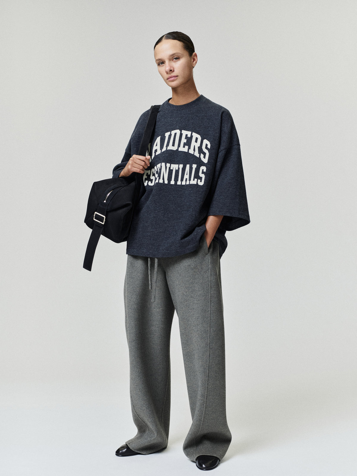 Raiders Merch Tee charcoal oversized short sleeve shirt with white Raiders Essentials collegiate lettering styled with wide leg gray pants and a shoulder bag in a Tops look