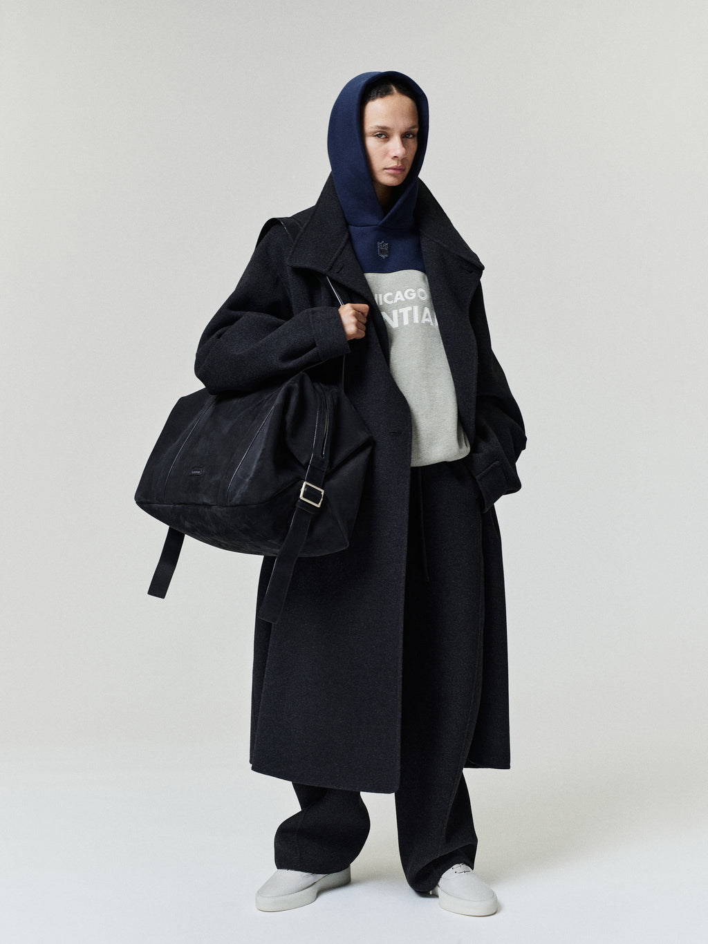 Bears 90s Relaxed Hoodie layered under a long black overcoat with loose black trousers white sneakers and a large shoulder bag on a model as a Tops fashion view