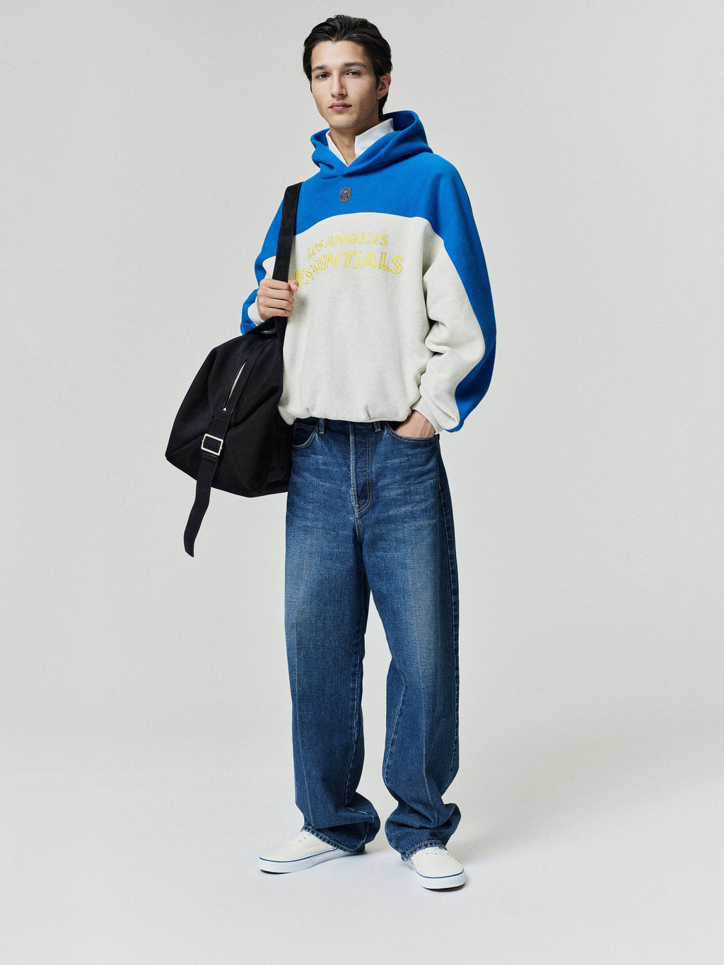 Rams 90s Relaxed Hoodie in blue and cream with yellow lettering styled with loose jeans white sneakers and a black shoulder bag on a model as a Tops fashion view