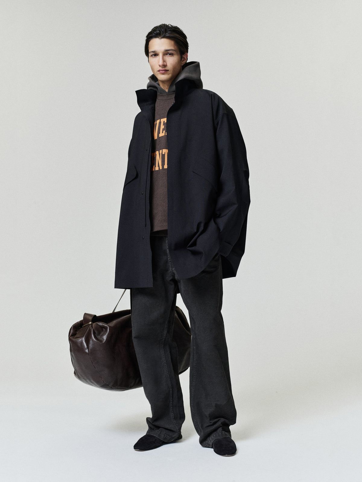 Browns Merch Tee layered under a black jacket with dark trousers and a brown duffle bag in a minimalist Fear of God Tops lookાન્ય
