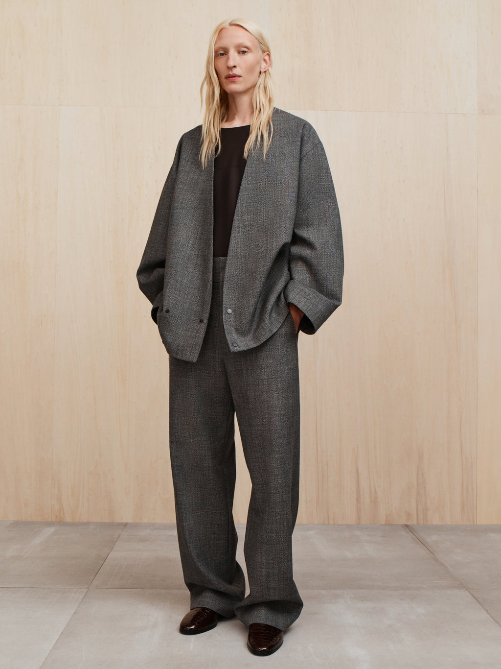 Woman wearing oversized gray checkered blazer with matching wide-leg trousers and black top against wood panel backdrop