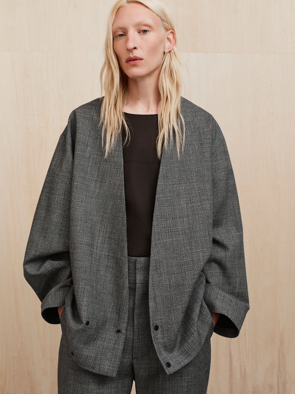 Model wearing oversized gray textured blazer with open front and matching trousers against beige backdrop