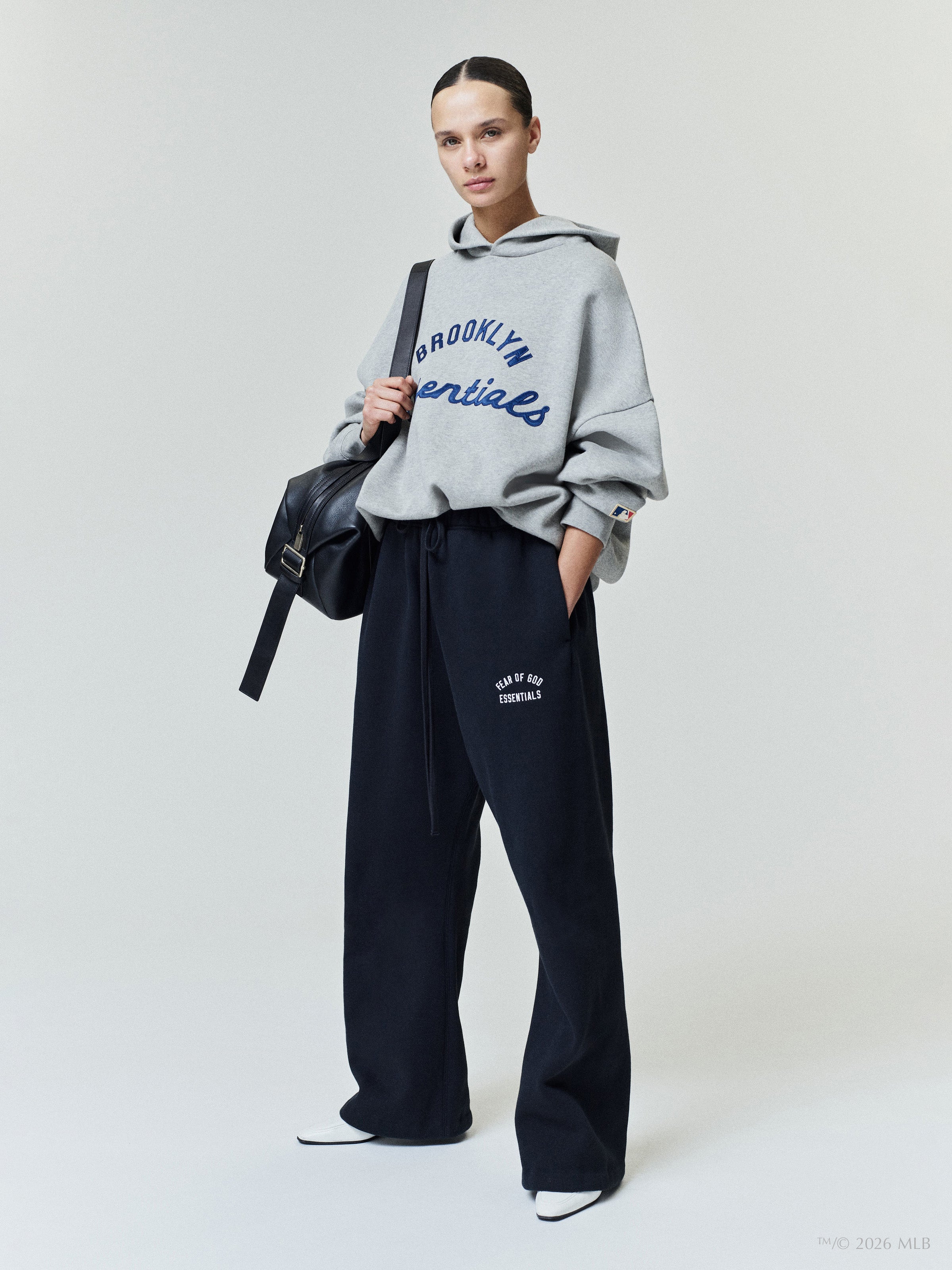 Woman wearing a loose gray hoodie with blue text paired with wide-leg black sweatpants and white shoes on a white background
