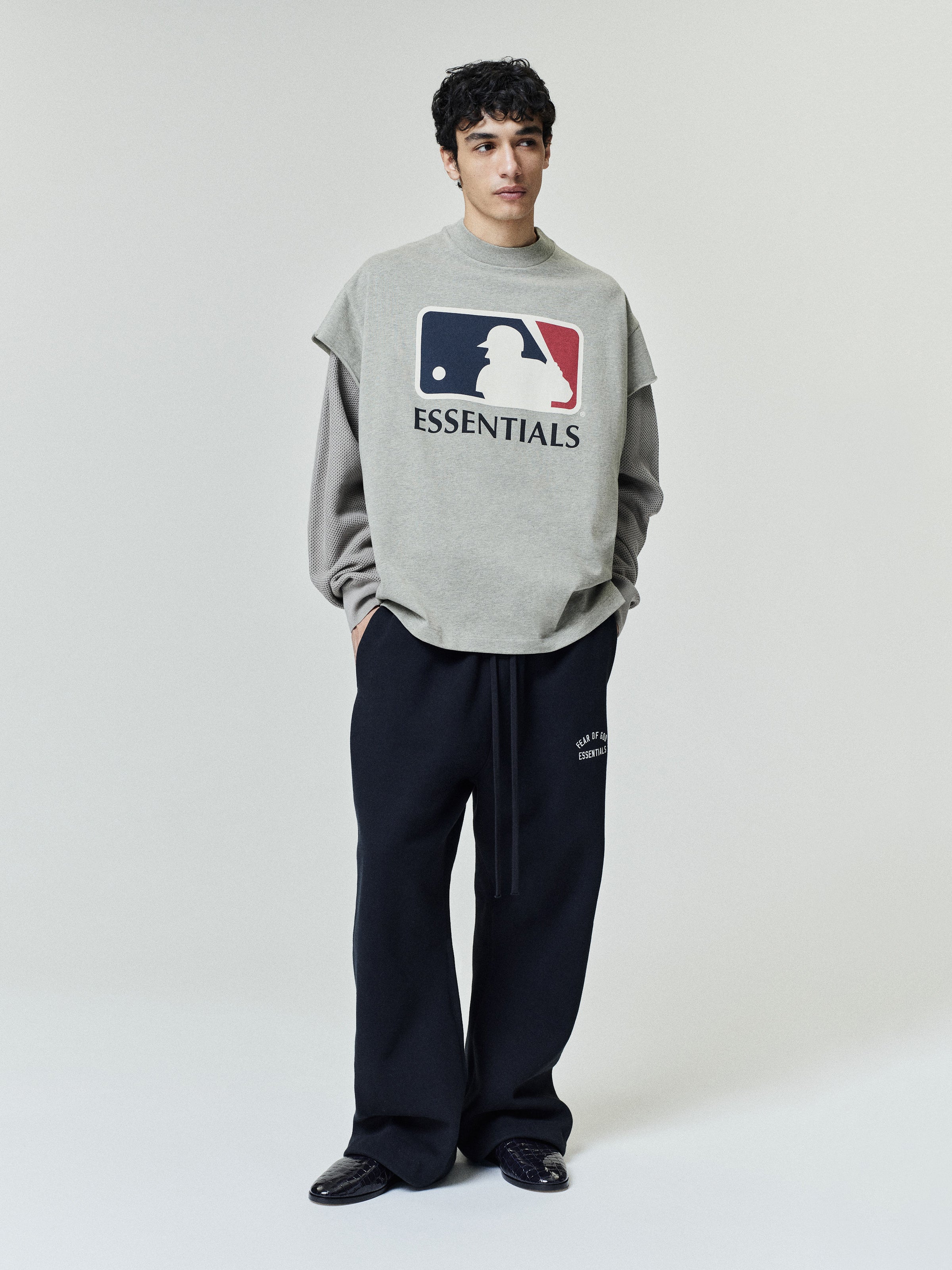 Model wearing Fear Of God X Franklin 90s Cutoff layered over a long-sleeve shirt, paired with relaxed black bottoms featuring subtle white text, styled with black shoes.