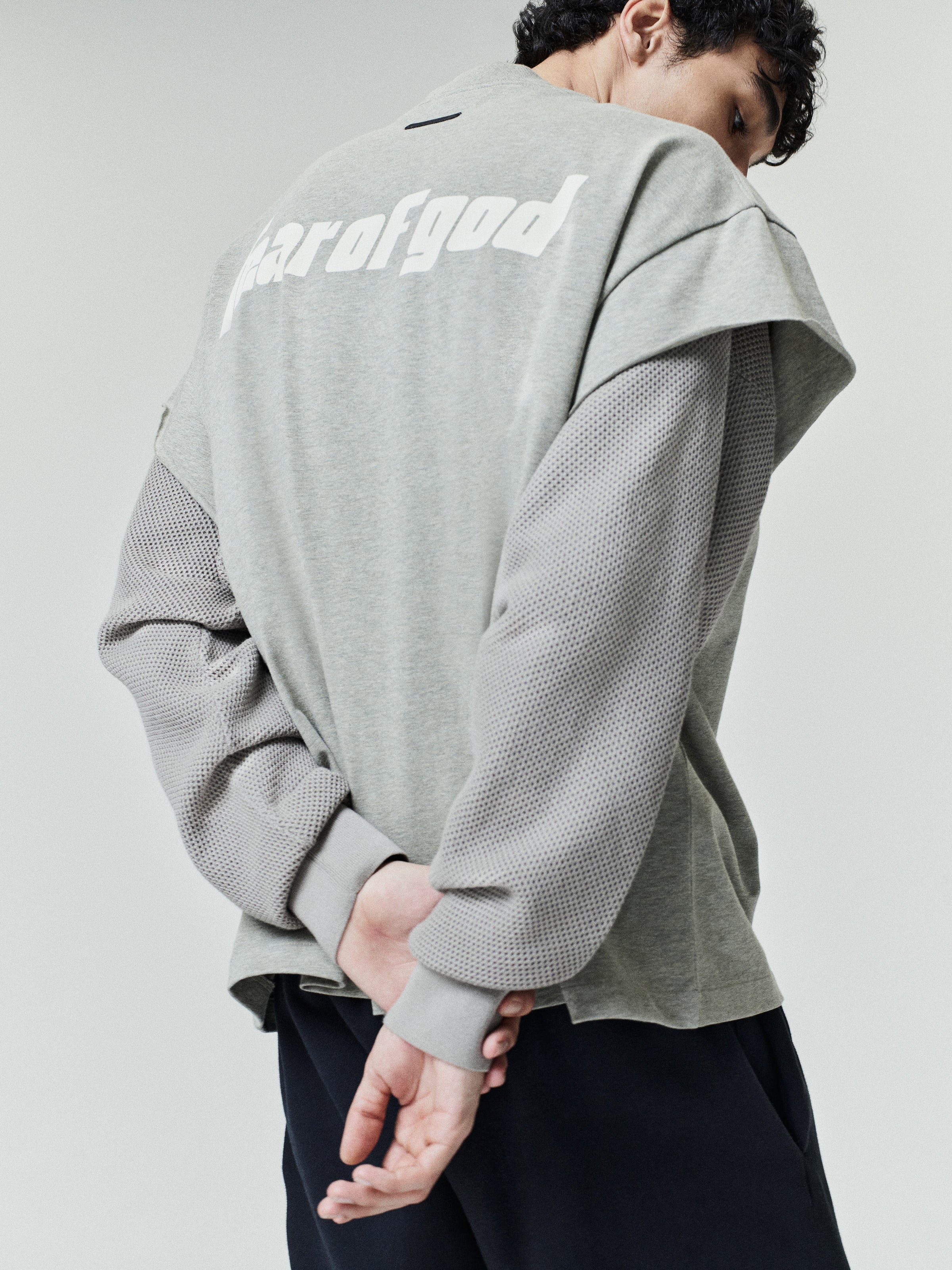 Rear view of a model wearing the Fear Of God X Franklin 90s Cutoff with a soft gray body and textured mesh long sleeves, paired with relaxed dark pants.
