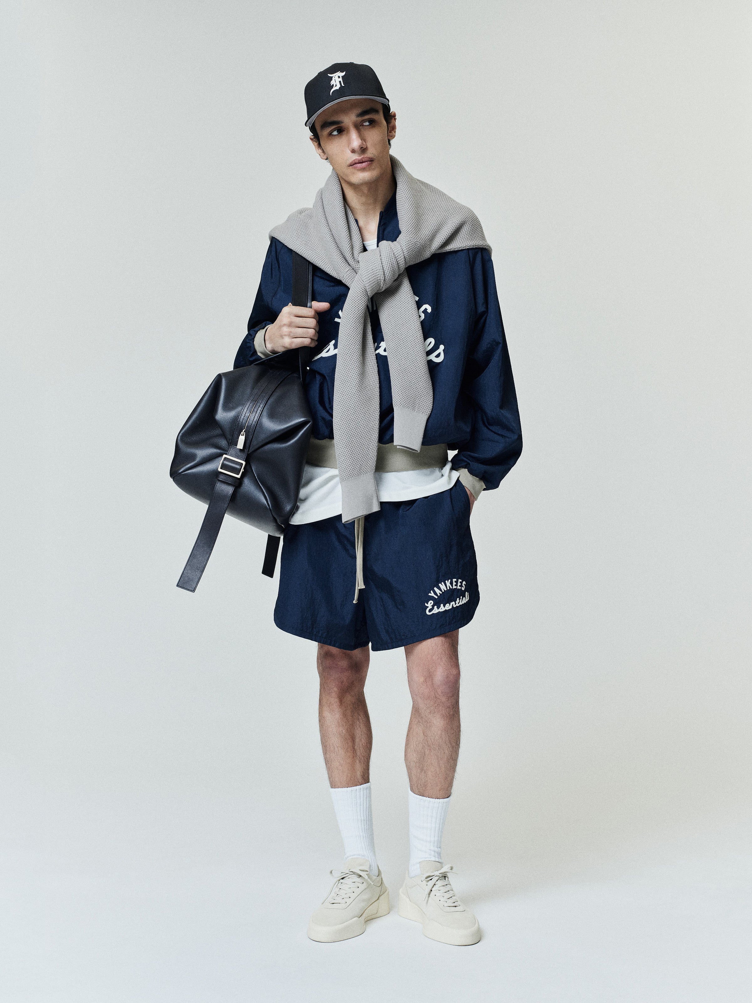 Yankees Gym Short in navy blue featuring a relaxed fit with white printed "Yankees Essentials" text on soft fabric, styled casually with a matching jacket, cap, and sneakers.