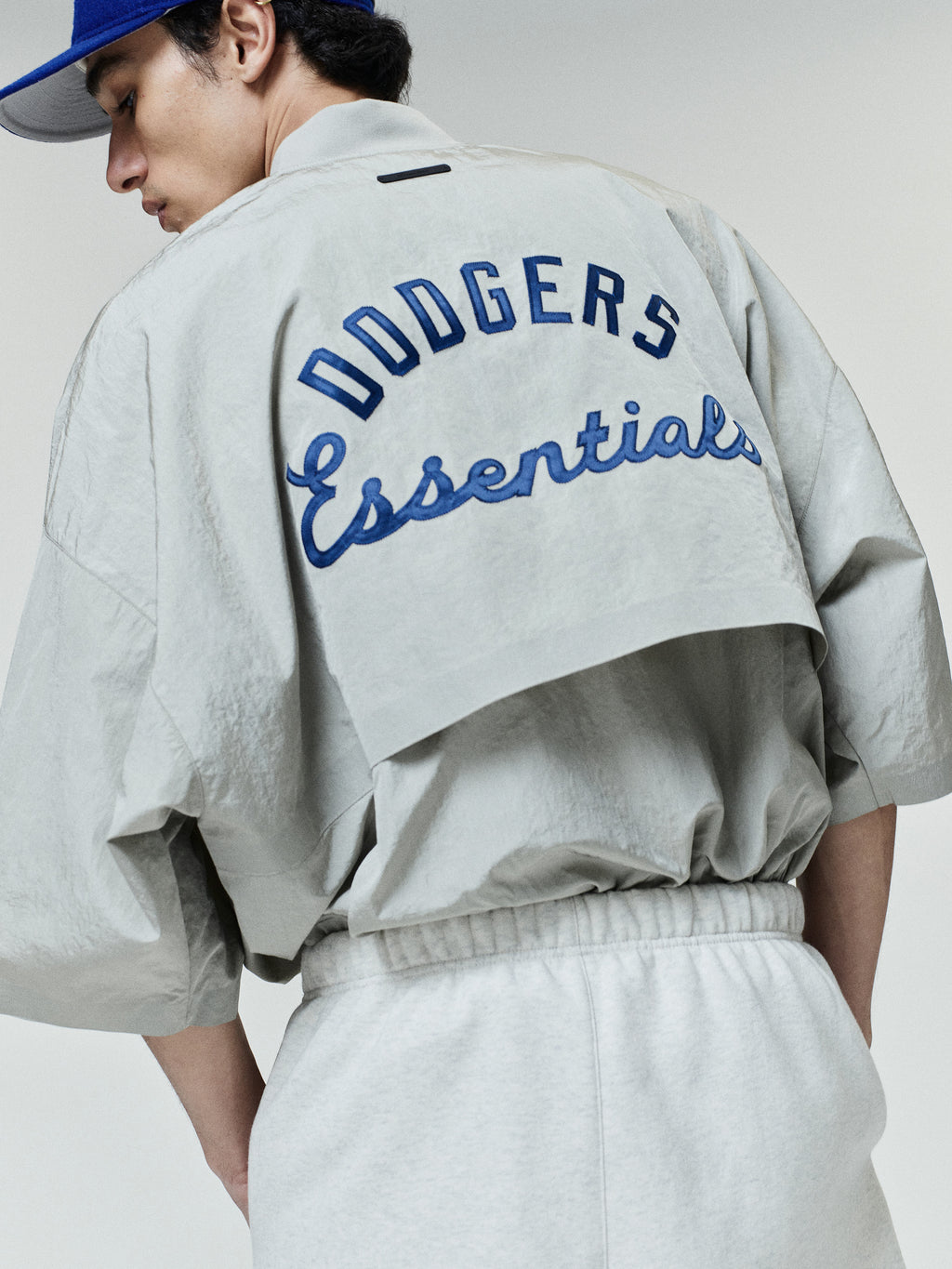 Back view of a light grey Dodger 3/4 Sleeve Pullover featuring bold blue "Dodgers Essentials" text embroidered on a cropped overlay with a relaxed fit and dropped shoulders.