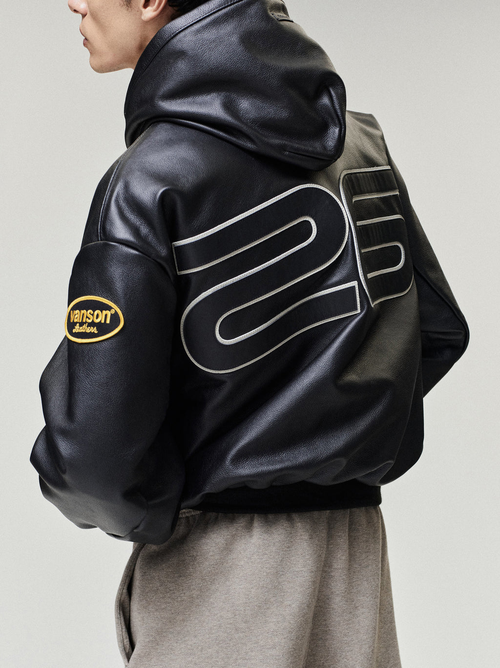 Person wearing a black leather jacket with branding on a plain background