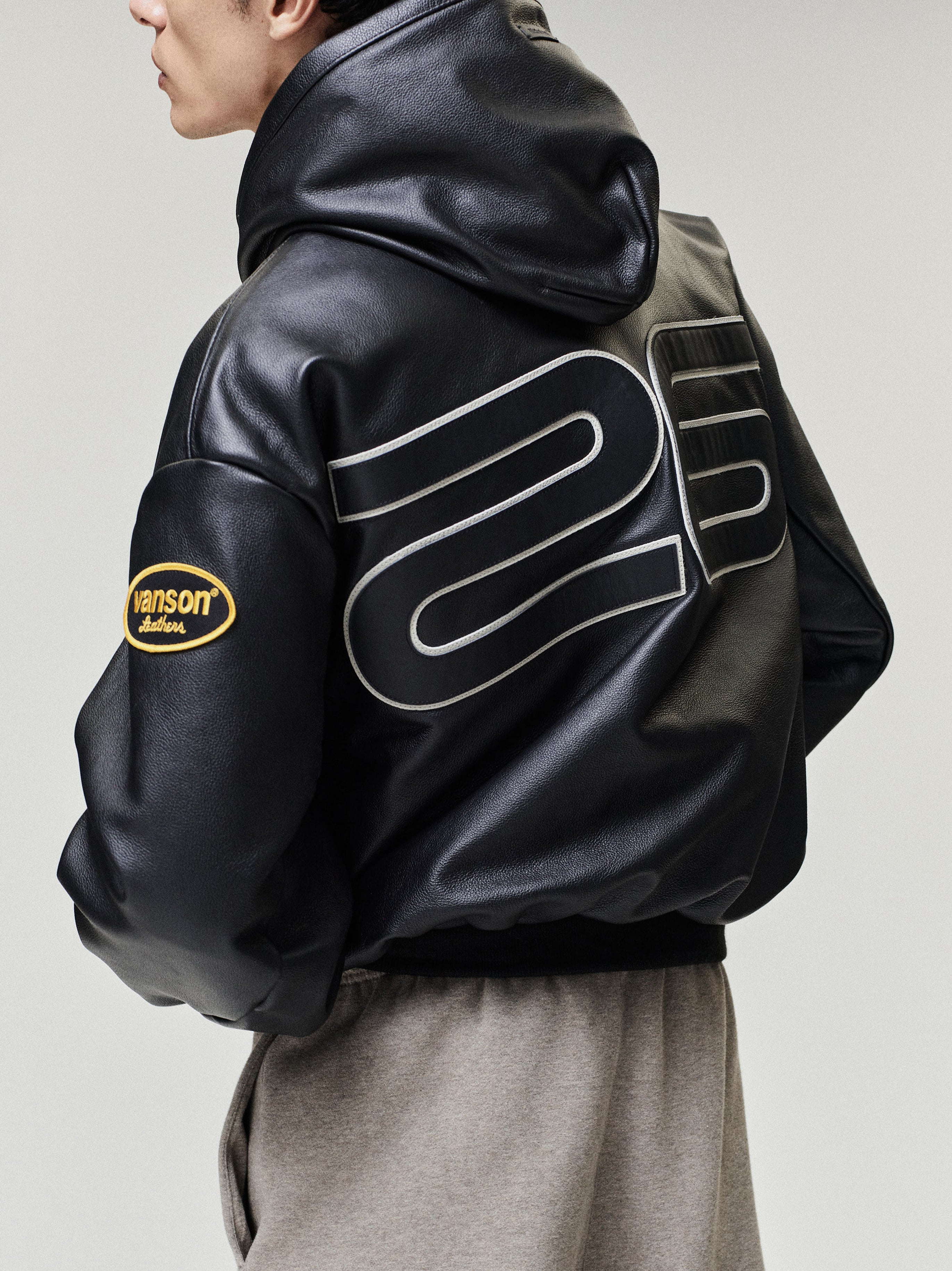 Person wearing a black leather jacket with branding on a plain background