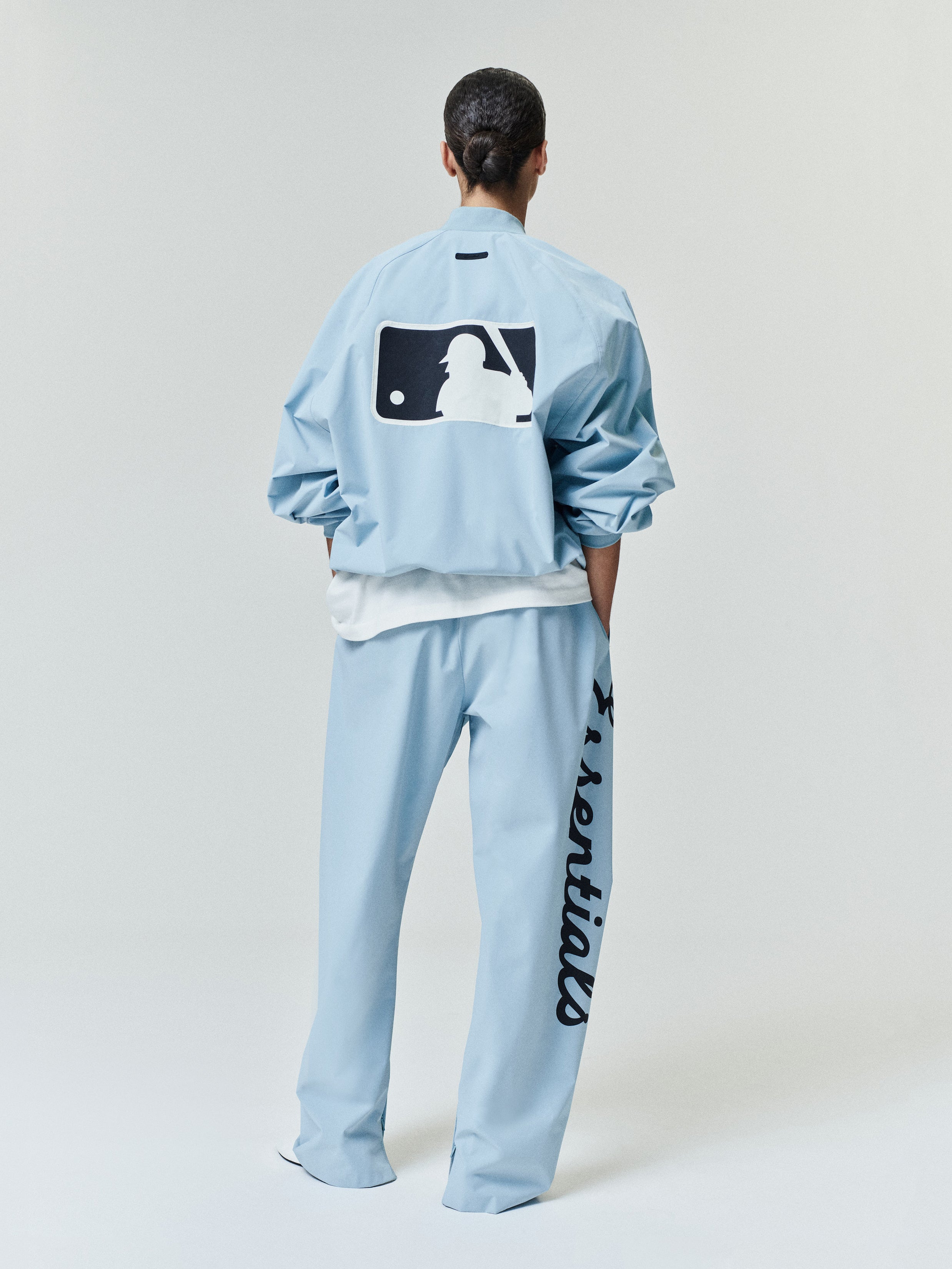 Back view of a model wearing a light blue Mlb Full Zip Bomber paired with matching pants featuring bold script down one leg, styled with a relaxed fit and crisp, clean lines.