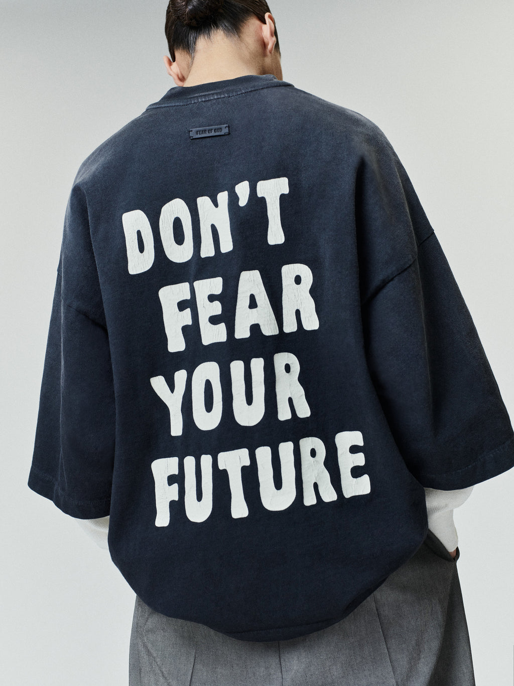 Person wearing an oversized dark washed t-shirt with large white block text on the back reading "DON'T FEAR YOUR FUTURE," paired with loose gray pants against a light background.