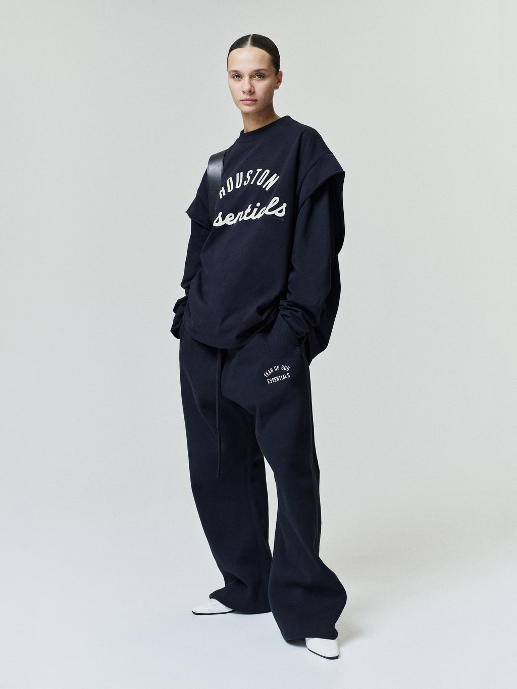 Front view of a person wearing a black layered top and loose black pants with white text on the chest and thigh, styled with white pointed shoes, part of the Astros 90s Cut Off collection.