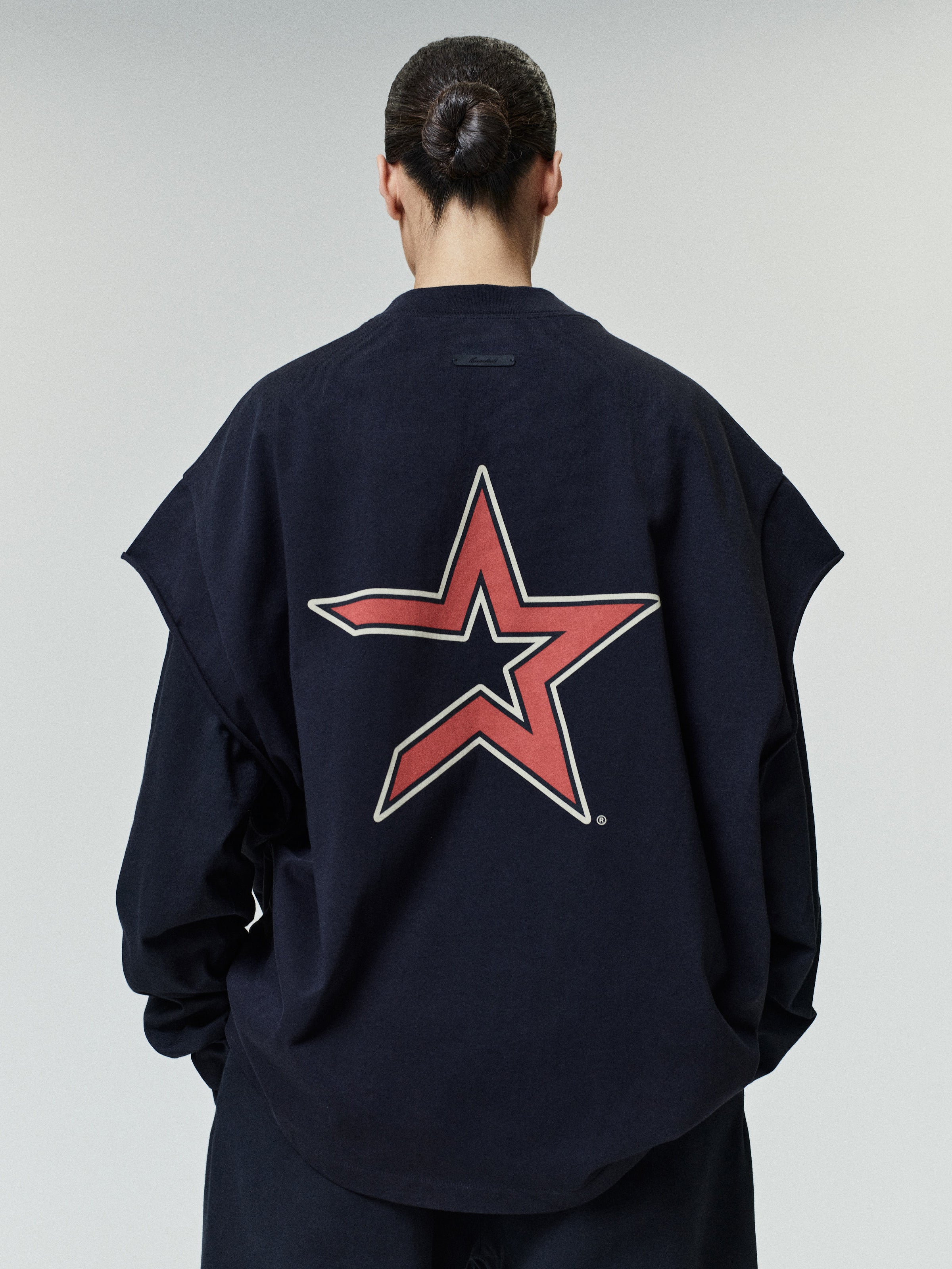 Rear view of a person wearing a navy oversized top featuring a large stylized red and beige star graphic centered on the back, part of the Astros 90s Cut Off collection.