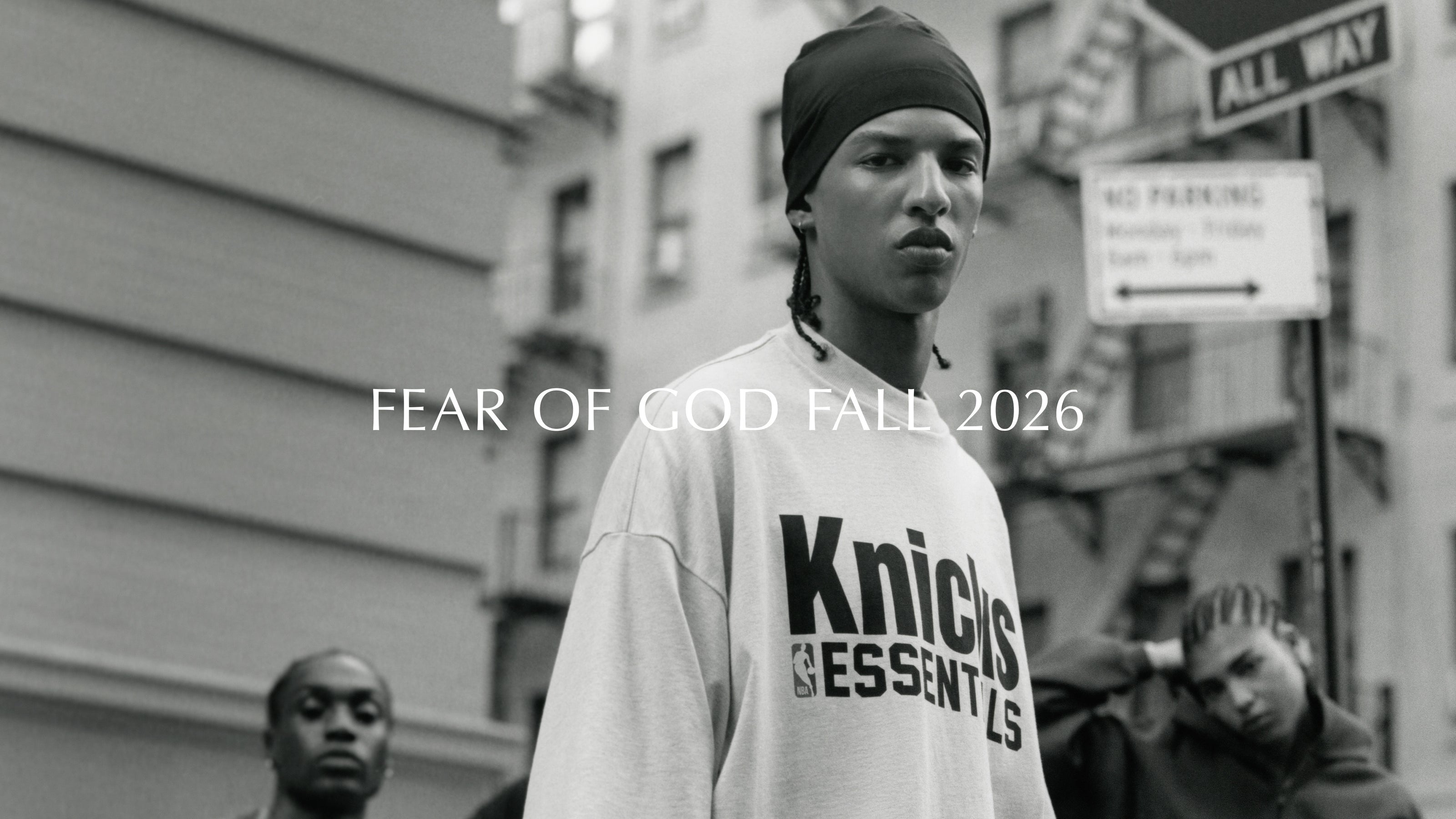 Black and white street portrait of a person wearing a head covering and Knicks Essentials sweatshirt with Fear of God Fall 2026 text overlay Tops