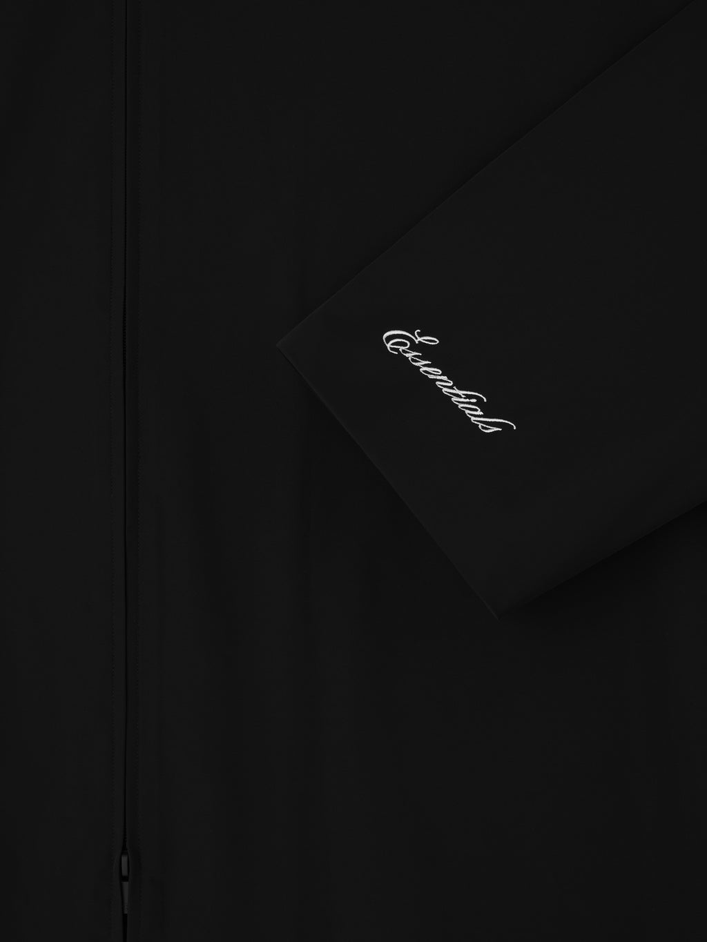 Close-up of black Sporty Nylon High Neck Jacket sleeve with white cursive Essentials logo embroidery and front zipper detail
