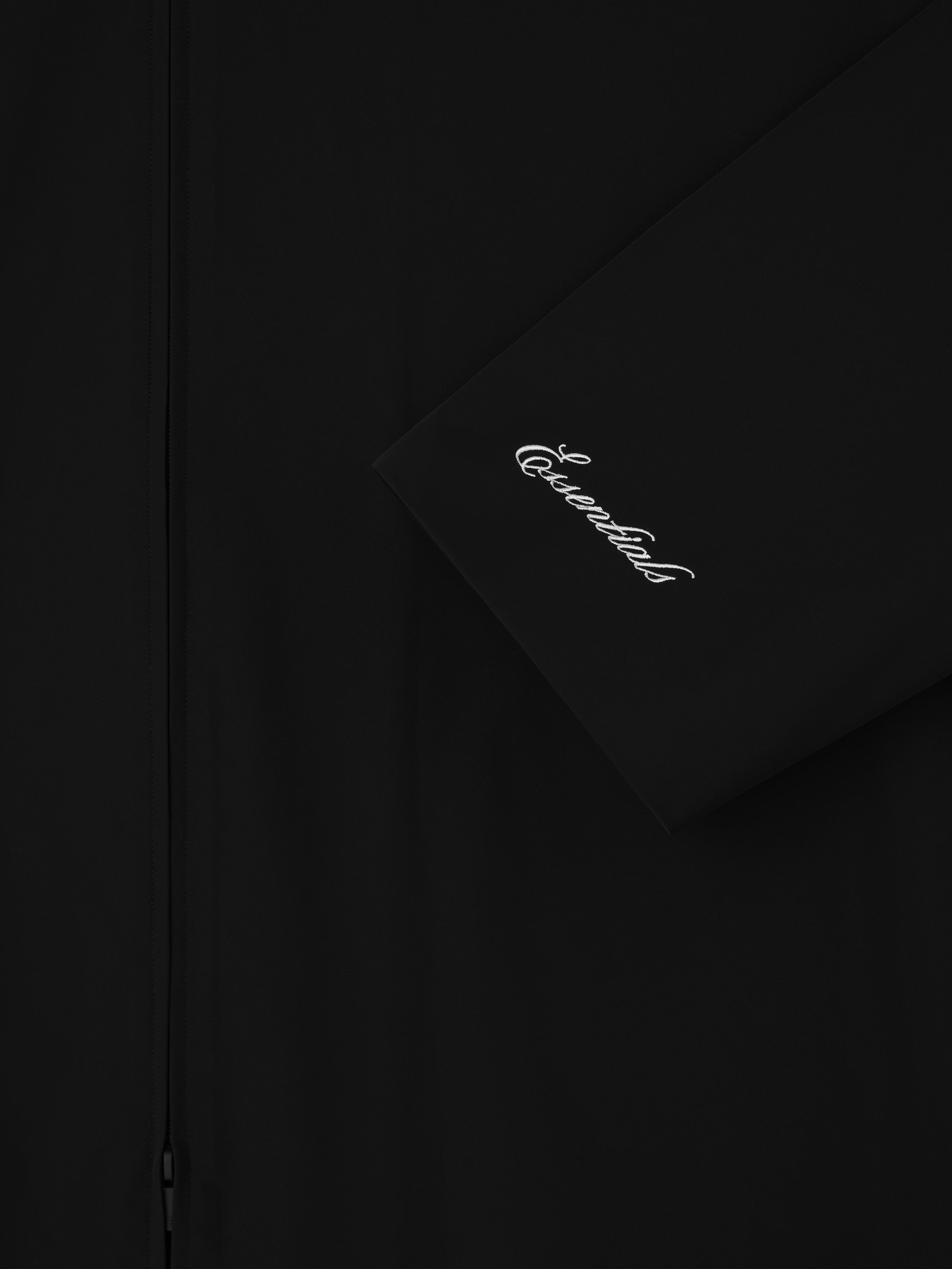 Close-up of black Sporty Nylon High Neck Jacket sleeve with white cursive Essentials logo embroidery and front zipper detail