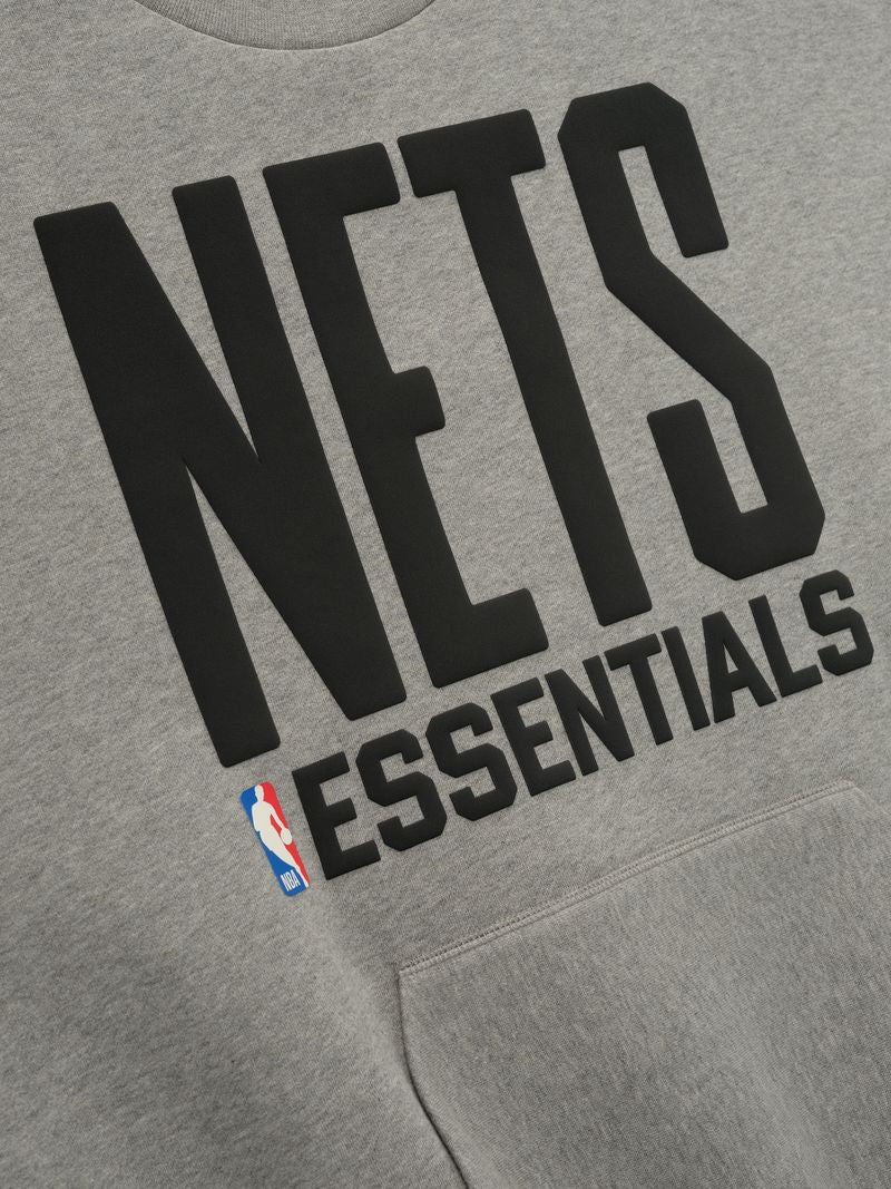 Close-up of grey Nets Sport Crewneck with large black NETS lettering, ESSENTIALS text, and NBA logo above kangaroo pocket