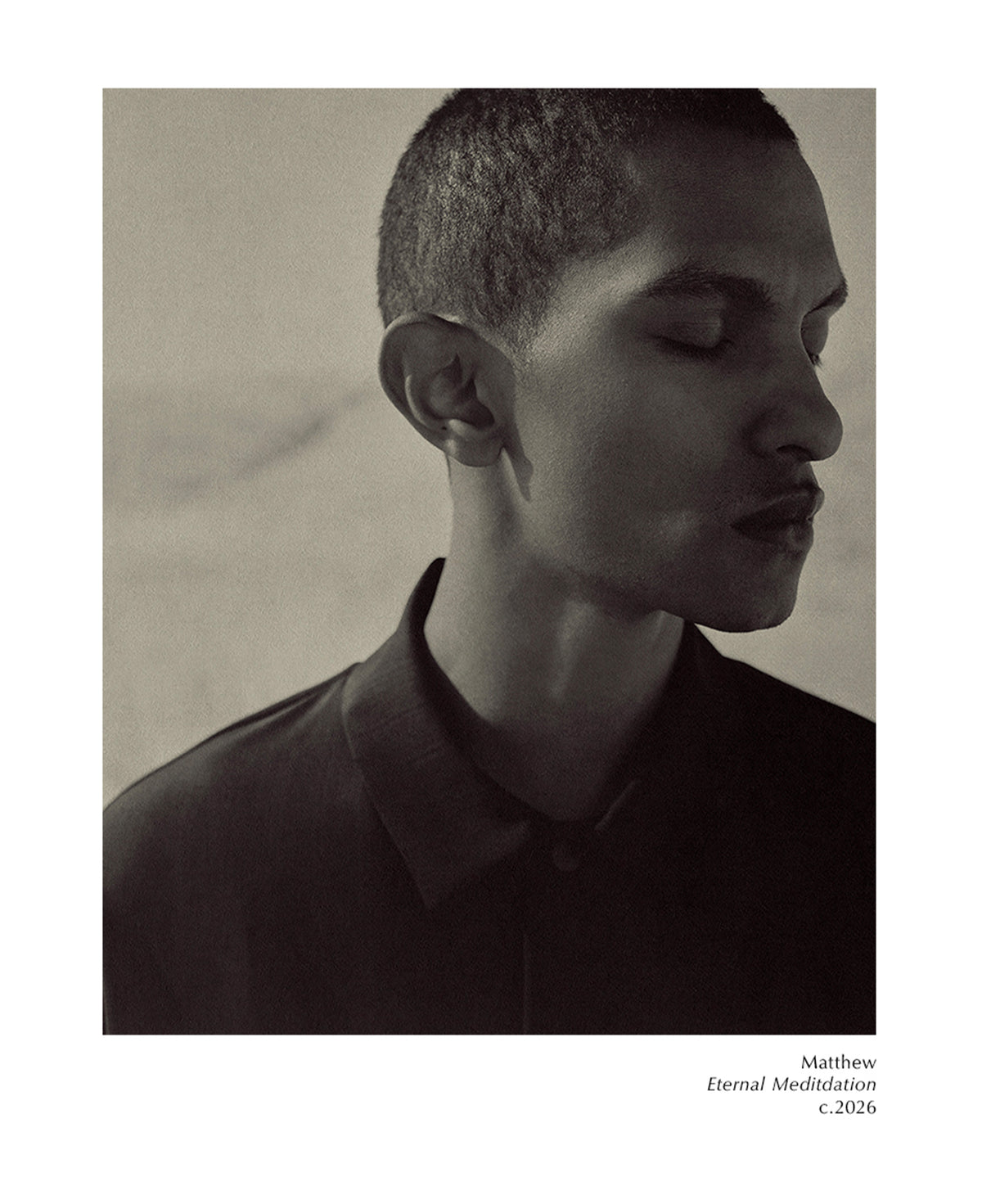Monochrome side profile of a young man with closed eyes wearing a dark collared top against a softly textured background with small editorial text below