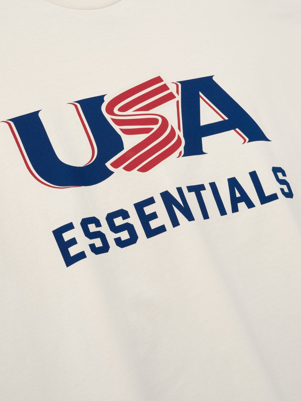 Close-up of cream-colored fabric with bold blue and red "USA" and navy "ESSENTIALS" text printed on front center